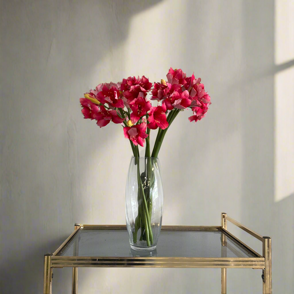 Artificial pink amaryllis stems arranged in a clear glass vase for styling purposes only