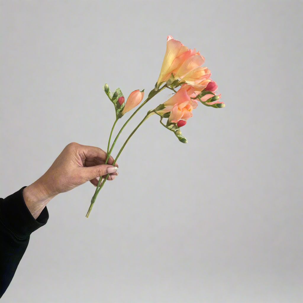 Artificial rose pink–peach orchid stem being held in hand, featuring open orchid blooms and unopened buds on a natural-look stem