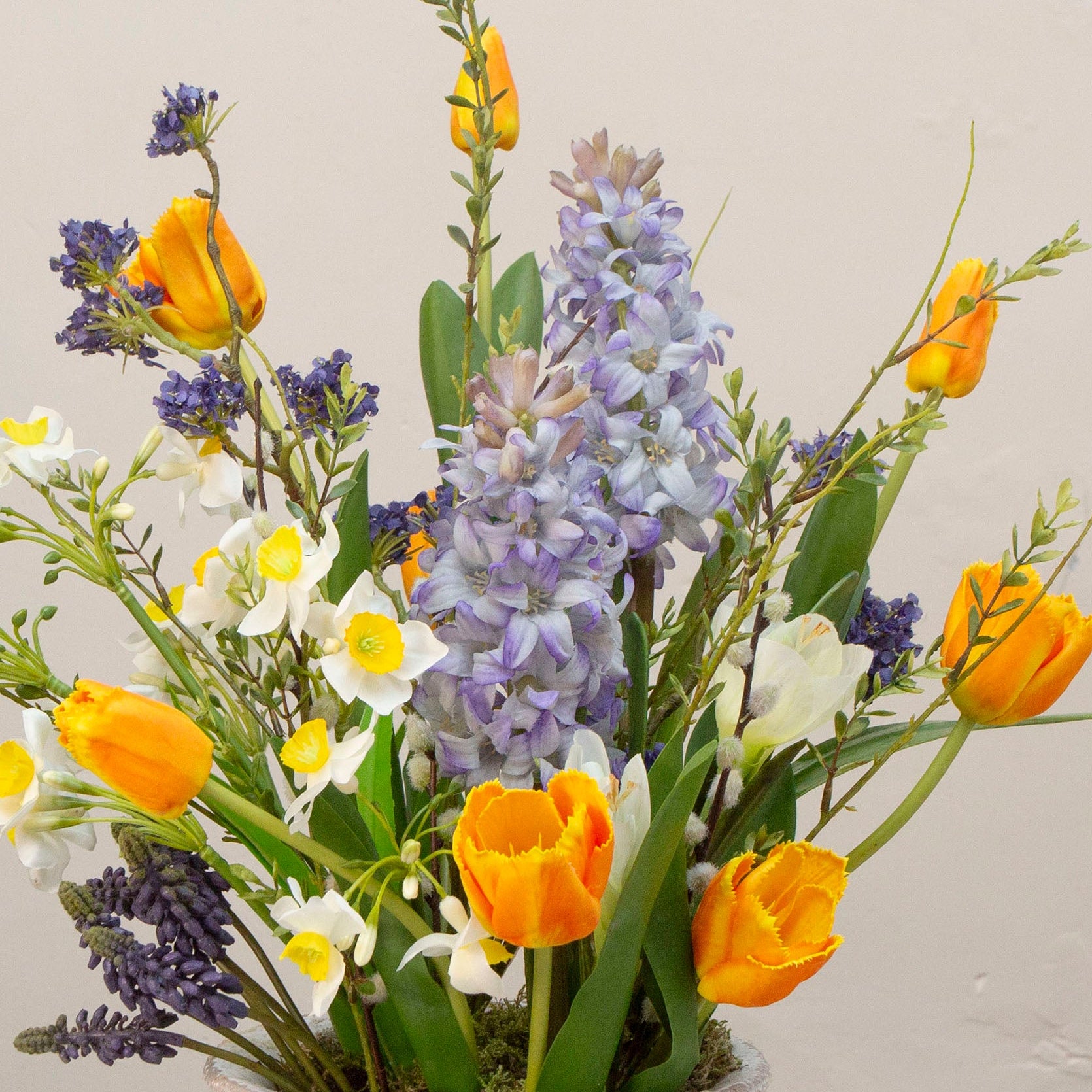 Artificial spring flower arrangement with daffodils and tulips in a white ceramic glazed urn