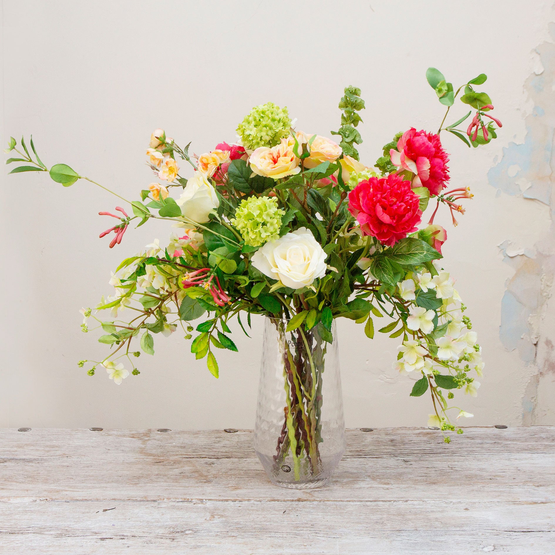 Artificial peach and lemon floral arrangement in a clear glass vase with roses, peonies, honeysuckle and viburnum