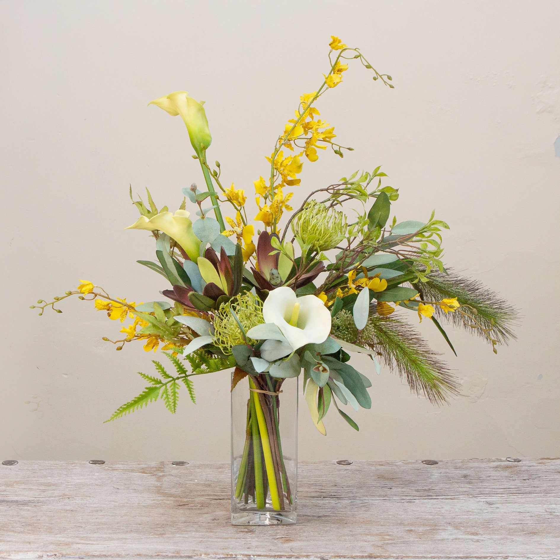 Artificial protea and calla lily arrangement with ferns, oncidium orchids and foliage in a clear glass vase