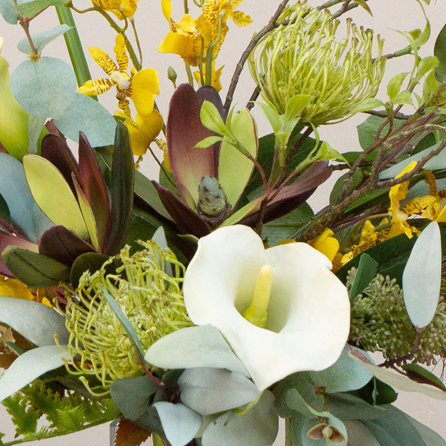 Artificial protea and calla lily arrangement with ferns, oncidium orchids and foliage in a clear glass vase