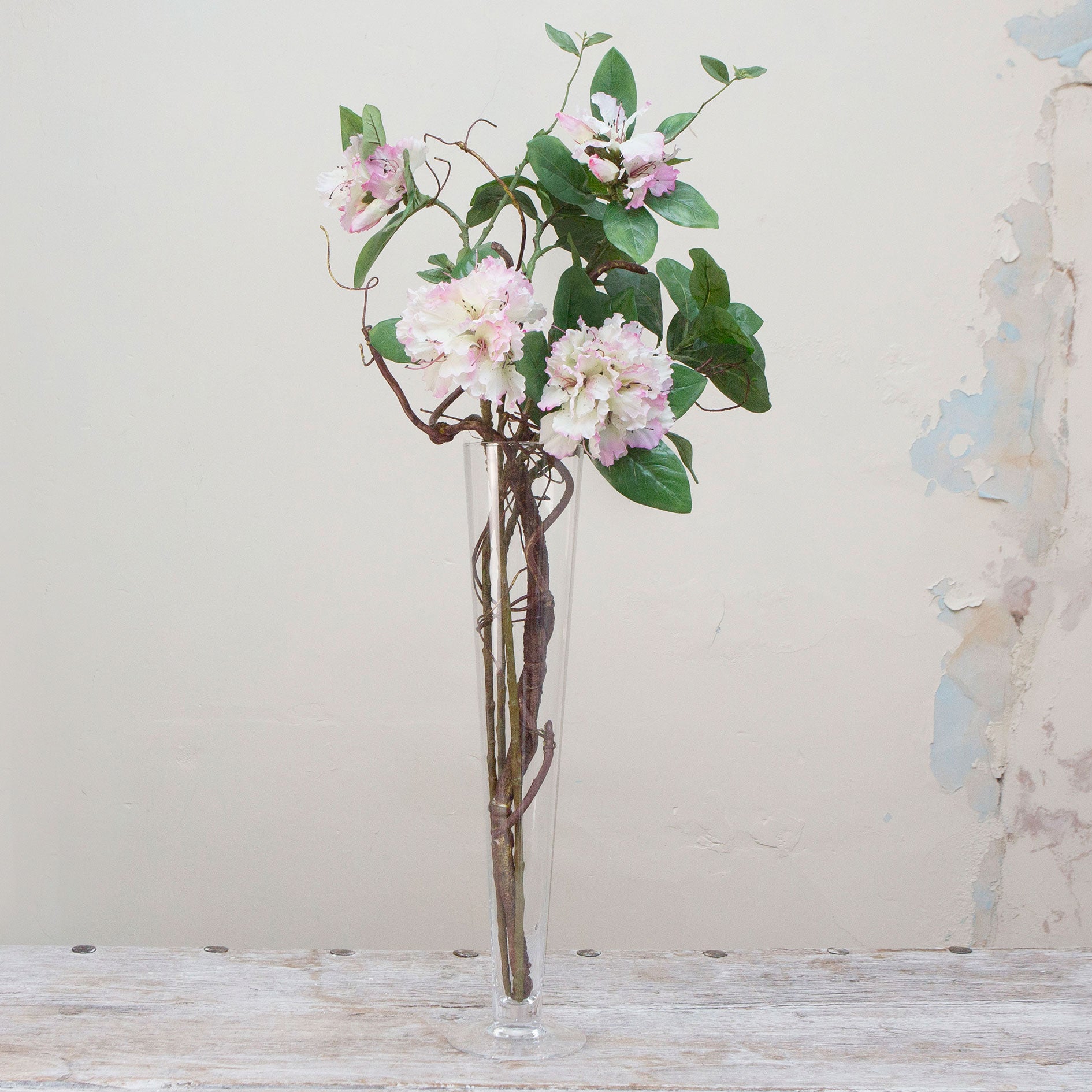 Artifical rhododendron and contorted willow arrangement in a tall conical glass vase