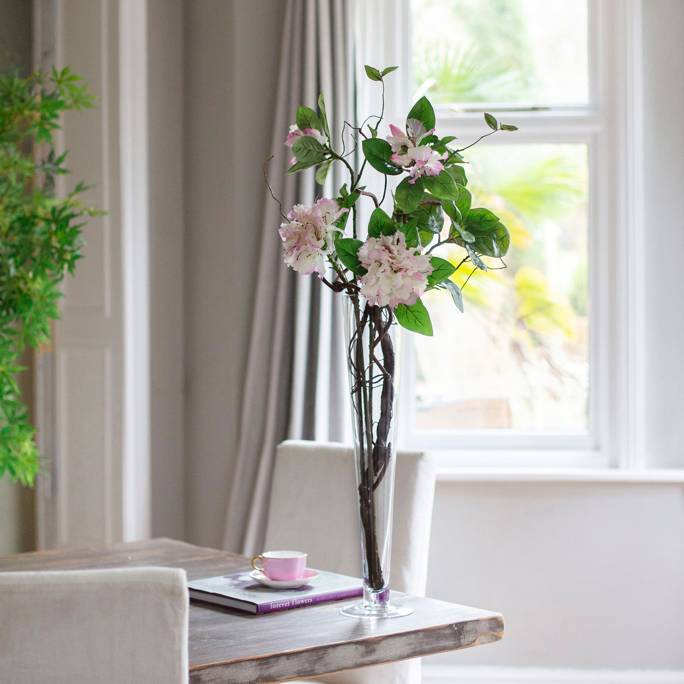 Artifical rhododendron and contorted willow arrangement in a tall conical glass vase