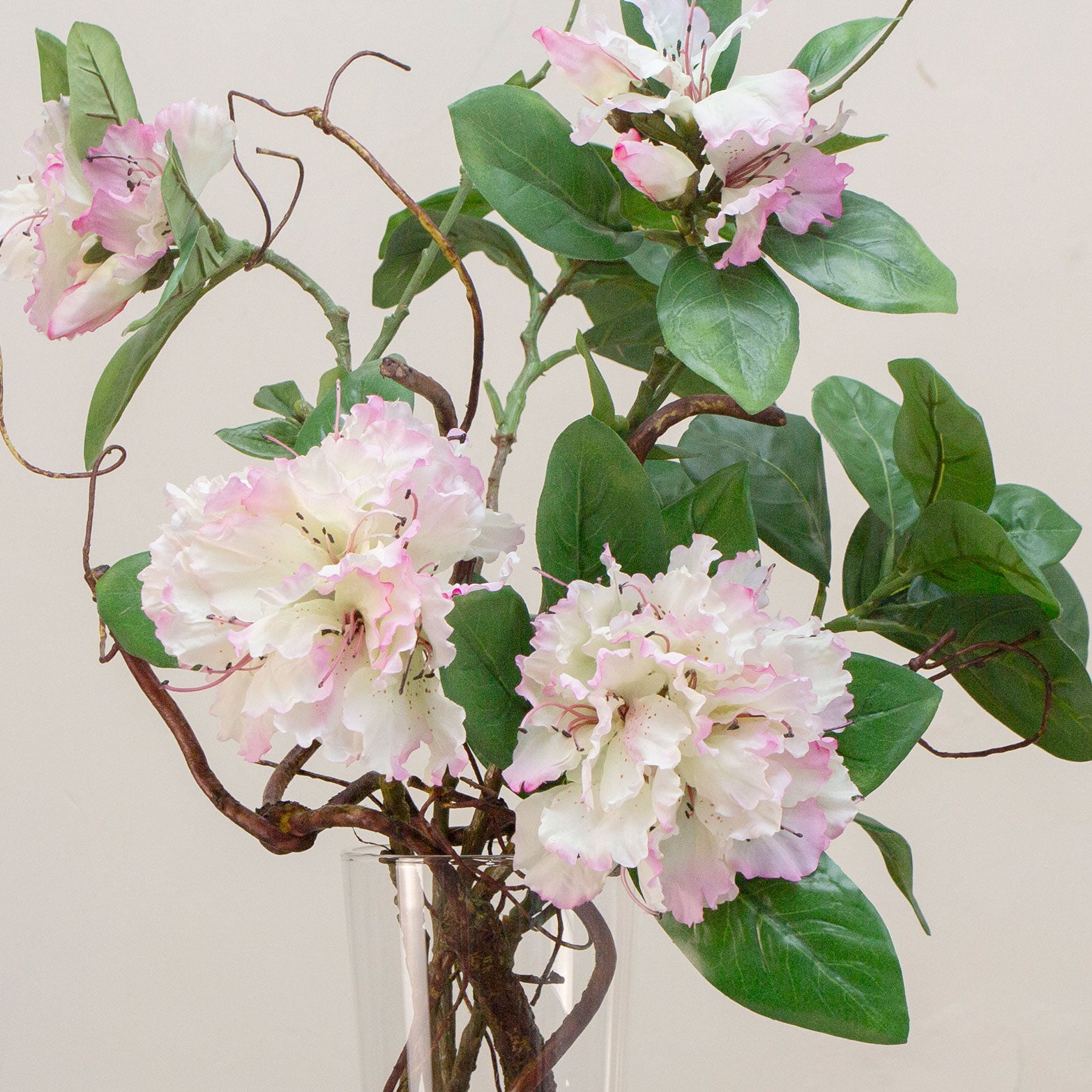 close up of artifical rhododendron and contorted willow arrangement in a tall conical glass vase