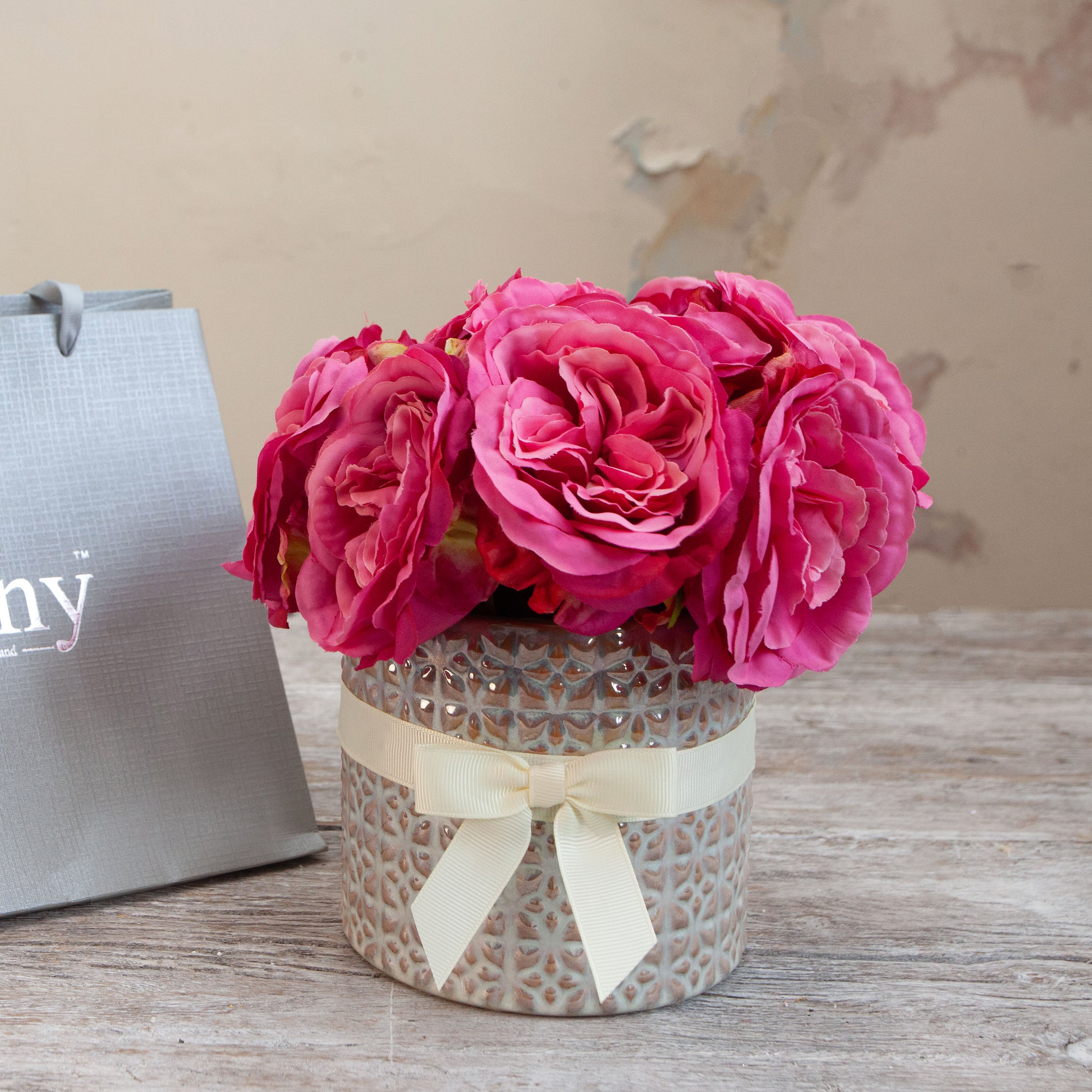 Close-up of artificial pink roses in a pearl-patterned pot with cream ribbon bow