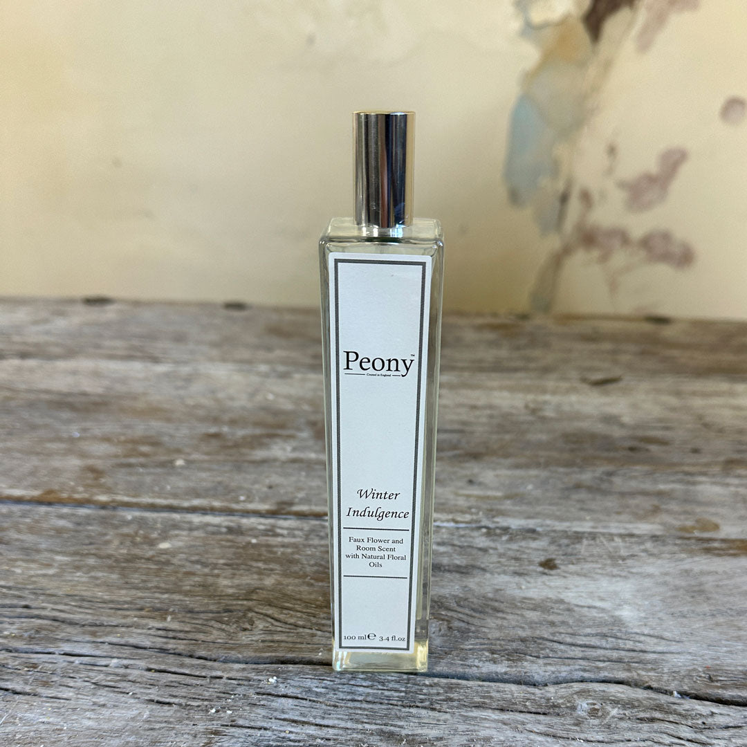 A bottle of 'Winter Indulgence' fragrance by Peony, placed on a wooden surface with a plain background.