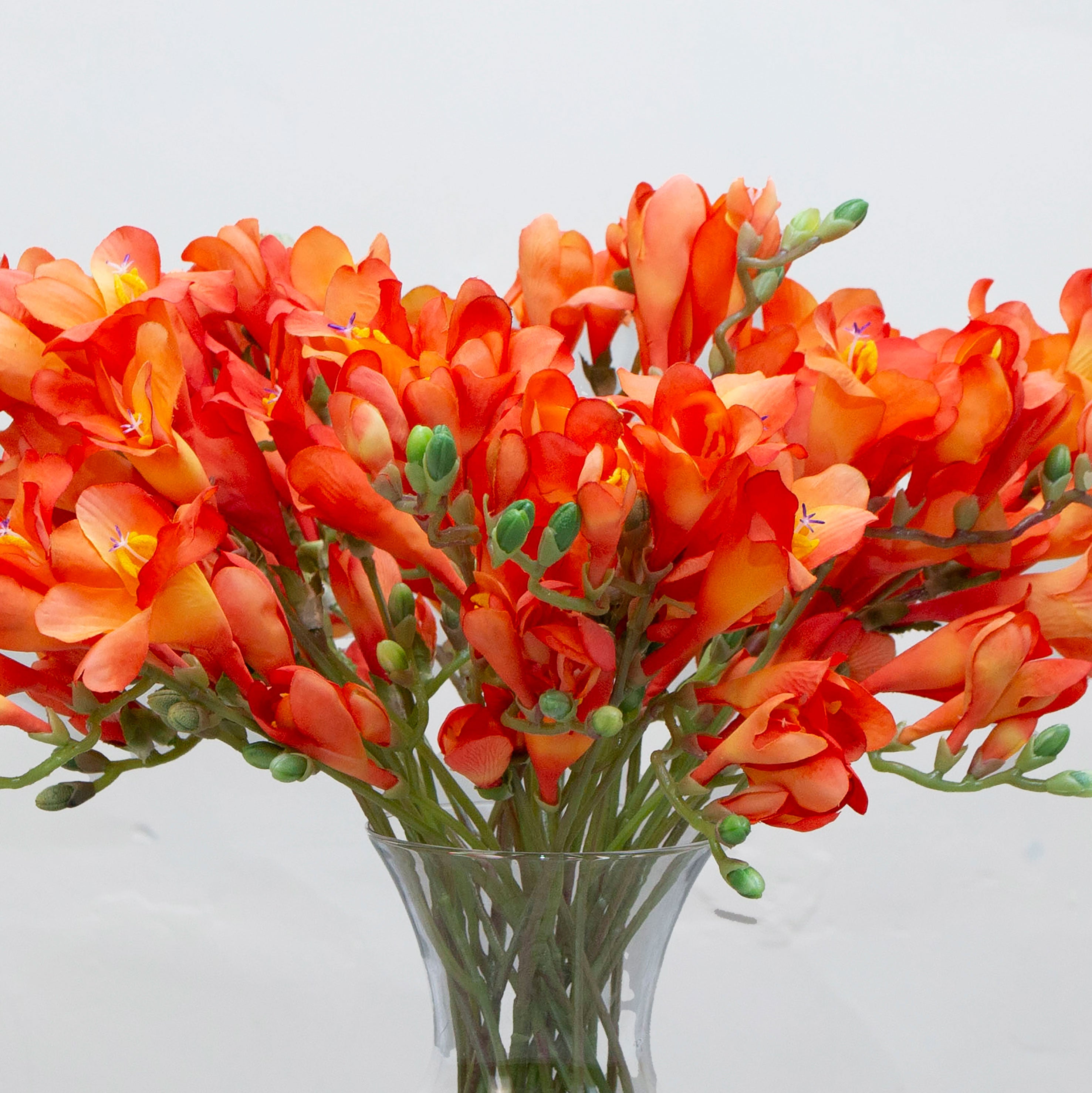 Close-up of artificial orange freesia flowers, showing warm flame-orange petals with soft tonal variation and realistic bud detail.