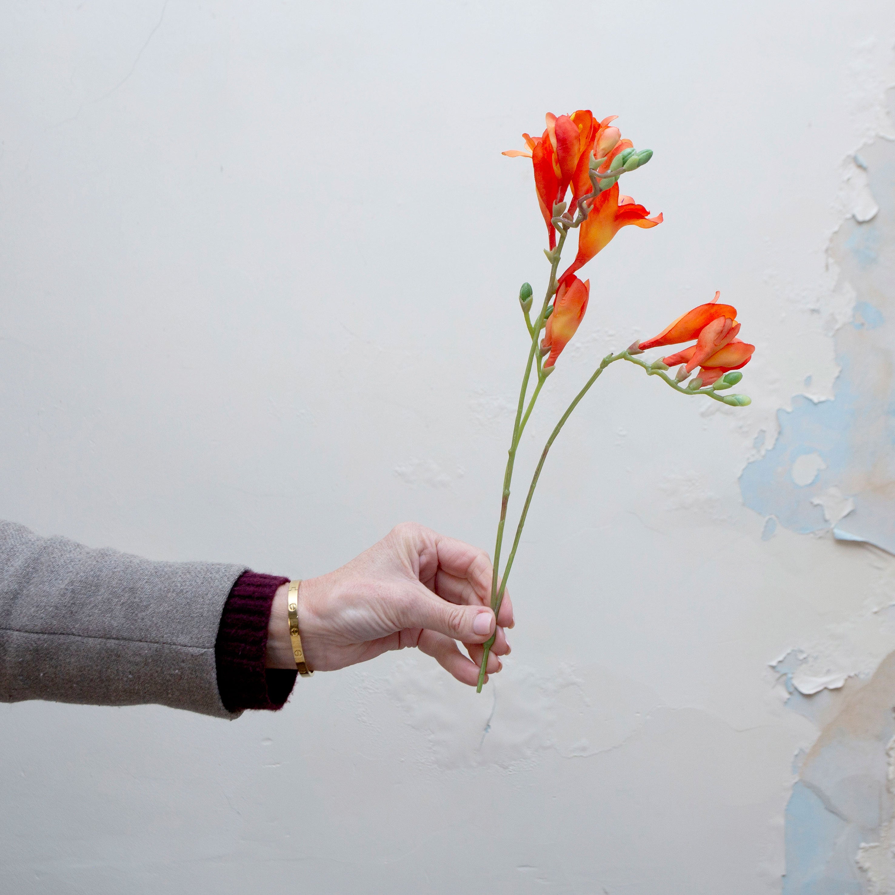 Artificial orange freesia stems being held in hand, featuring open trumpet-shaped blooms and green buds on natural-look stems