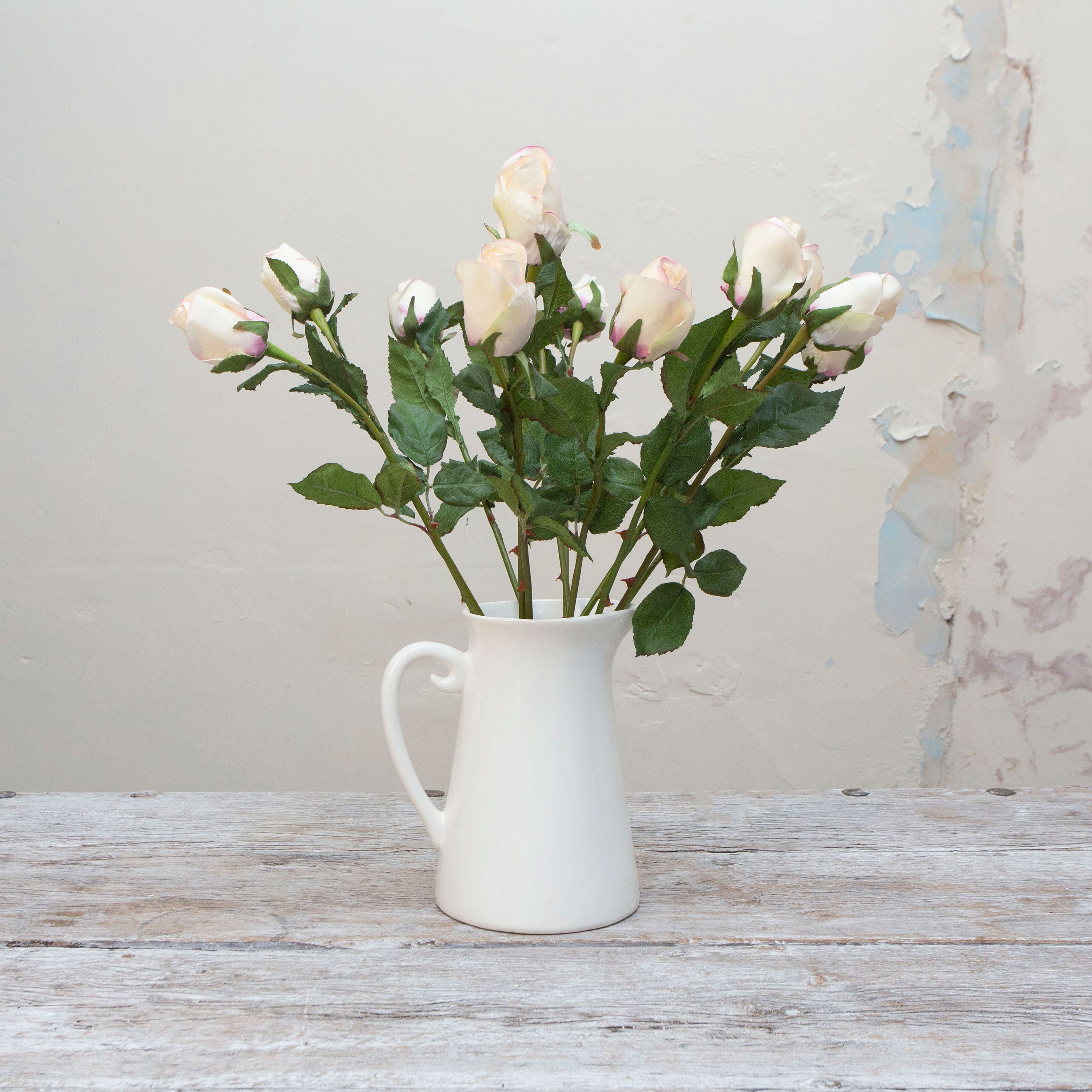 Artificial soft blush and cream open rose bud stems displayed together in a vase for styling purposes.