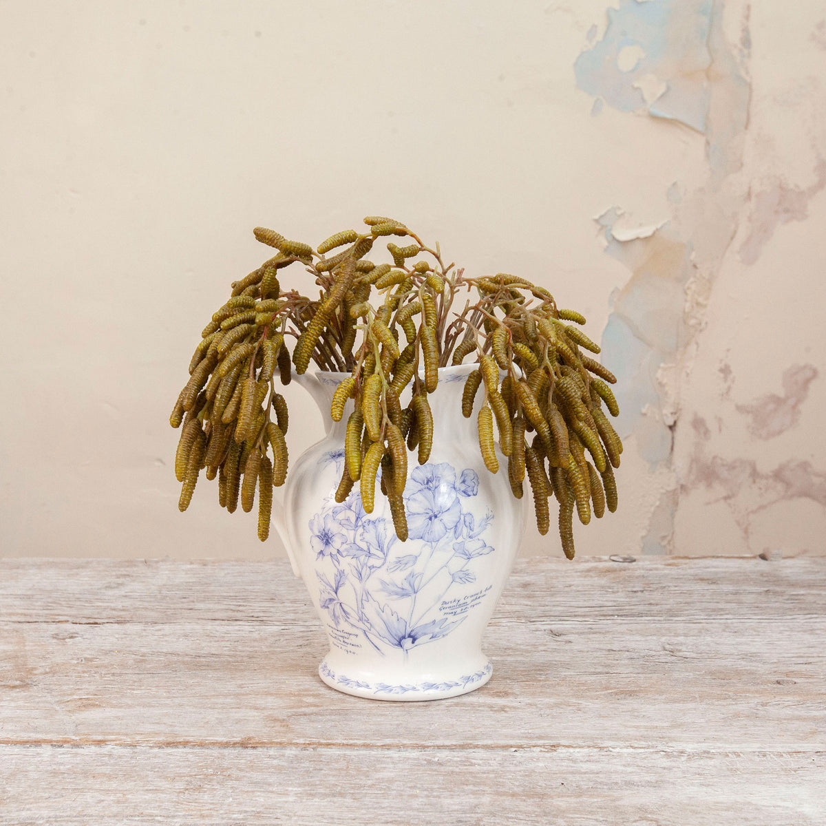 Artificial green birch foliage spray stem displayed in a blue and white floral ceramic vase