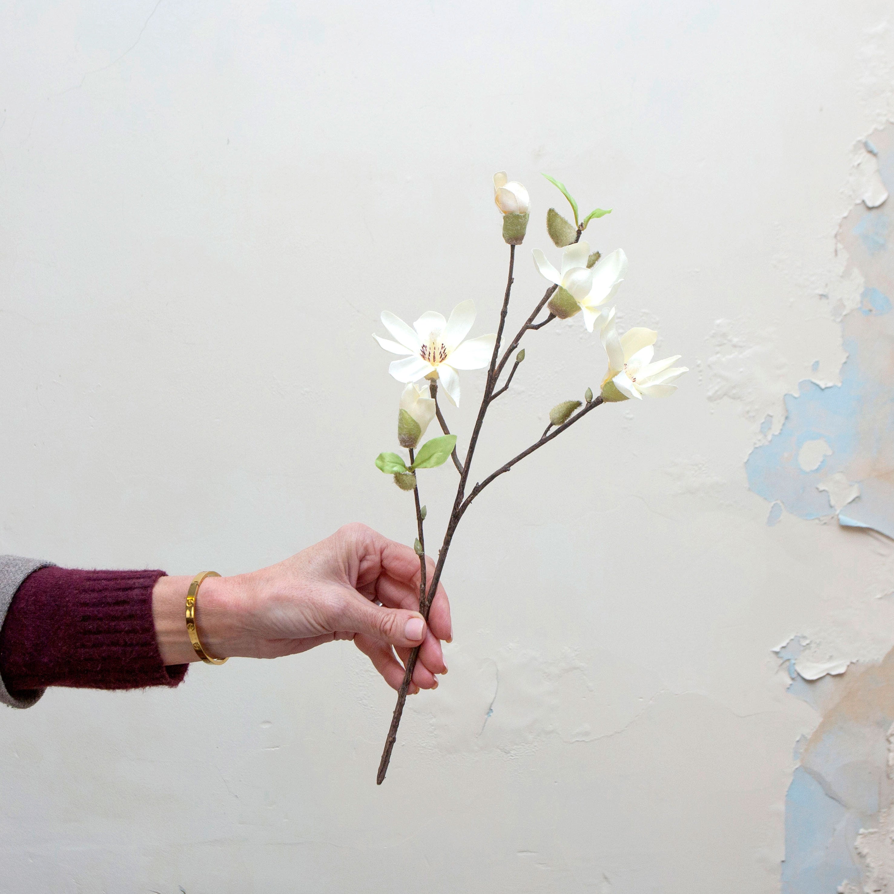 Artificial bridal white magnolia blossom spray stem held in hand, featuring open flowers and unopened buds on branching stems