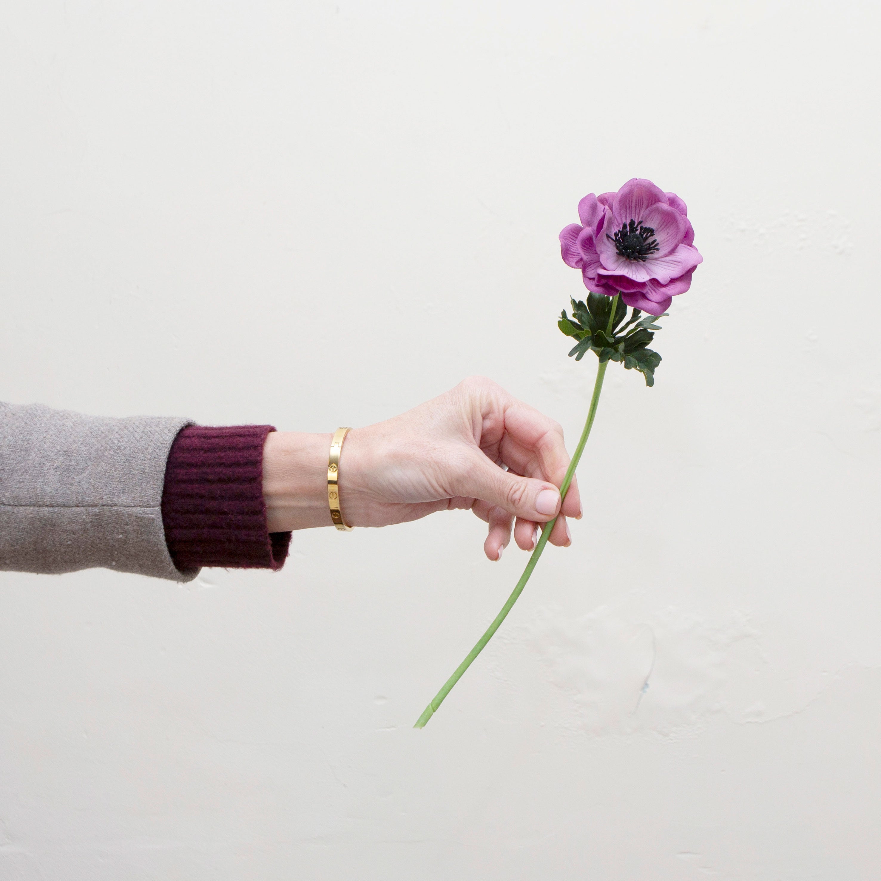 Artificial purple anemone stem held in hand, featuring an open bloom with dark centre and green stem