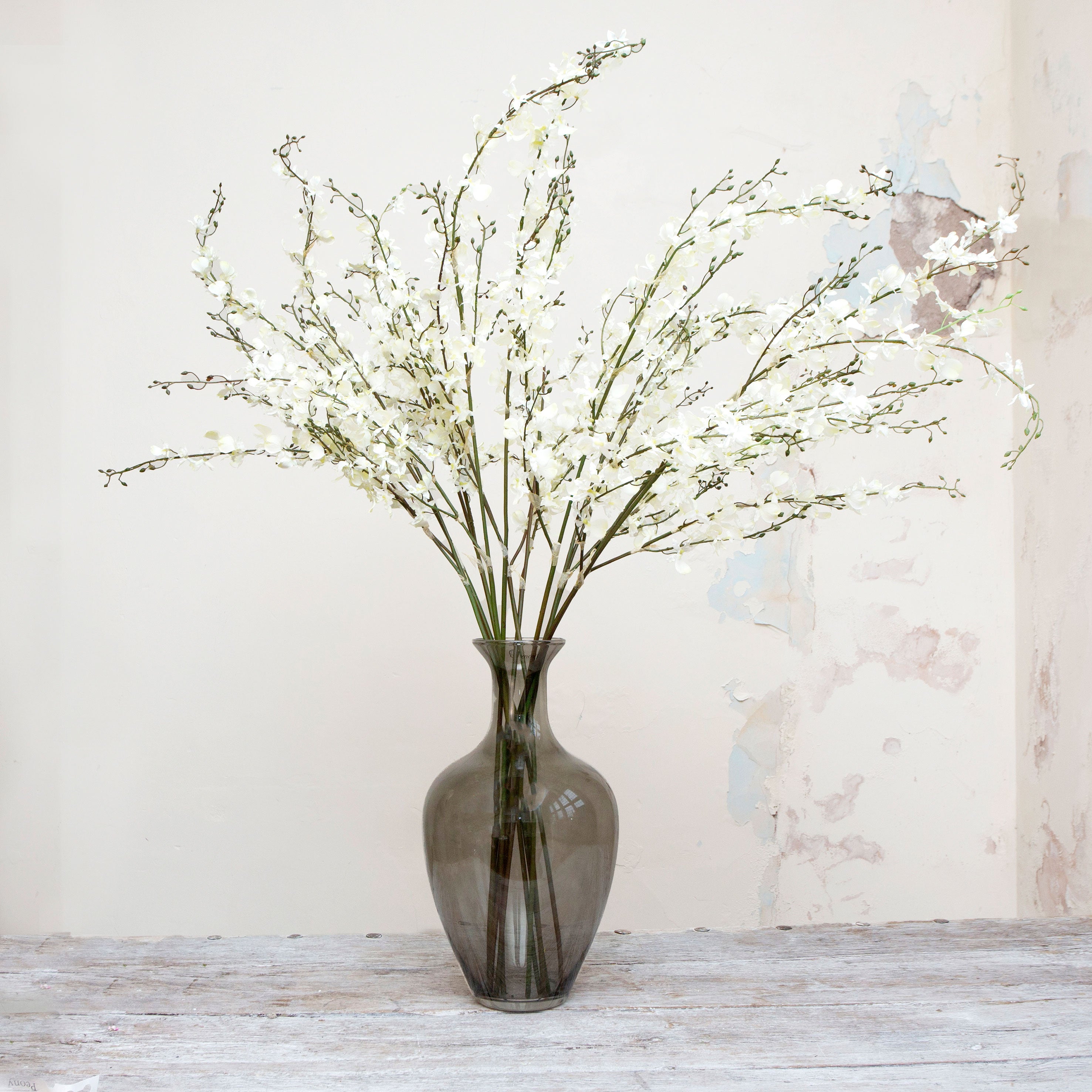 Artificial white dancing orchid stems displayed together in a vase for styling purposes.