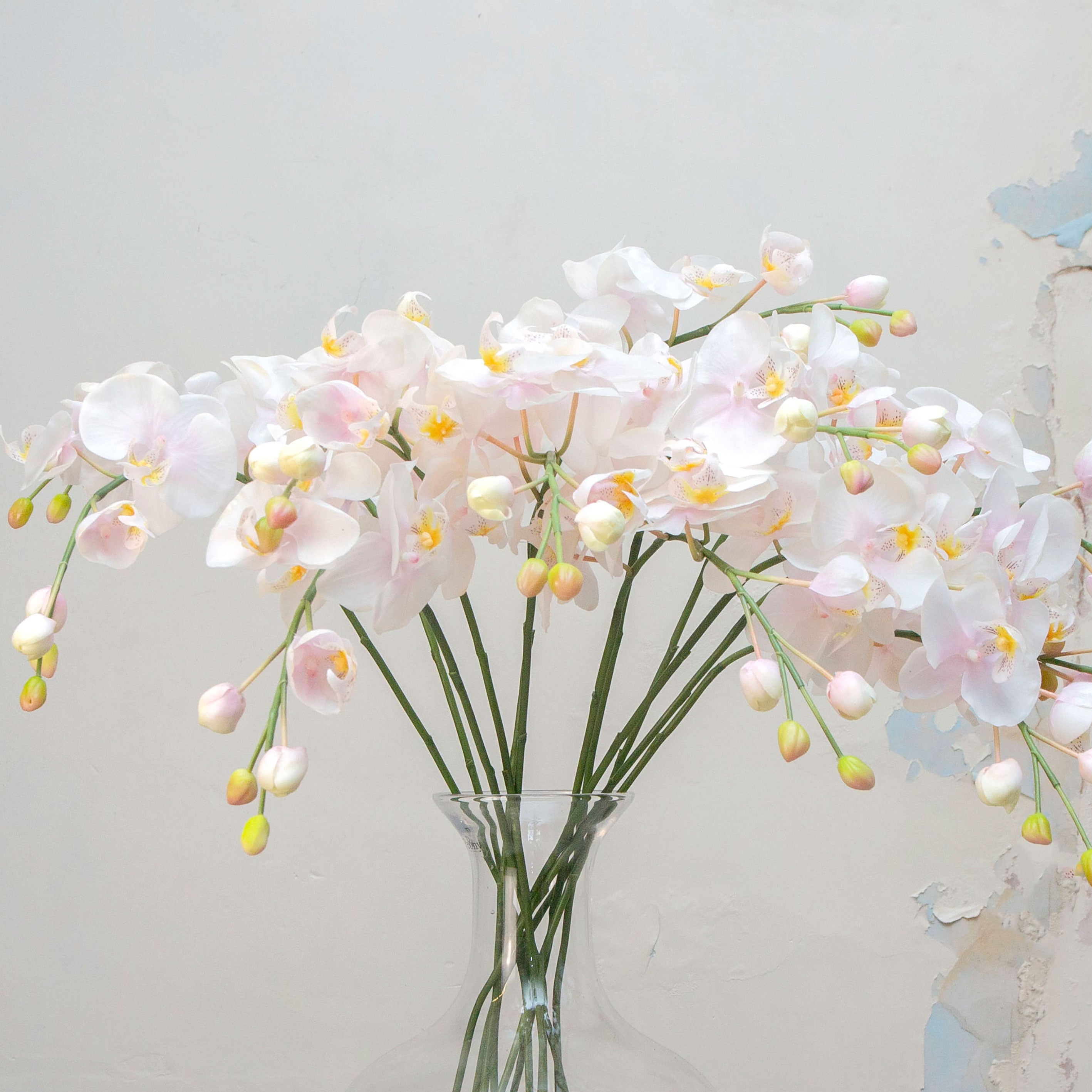 Close-up of artificial pale pink orchid flowers, showing soft blush-pink petals, warm yellow centres, gentle colour variation and natural veining.