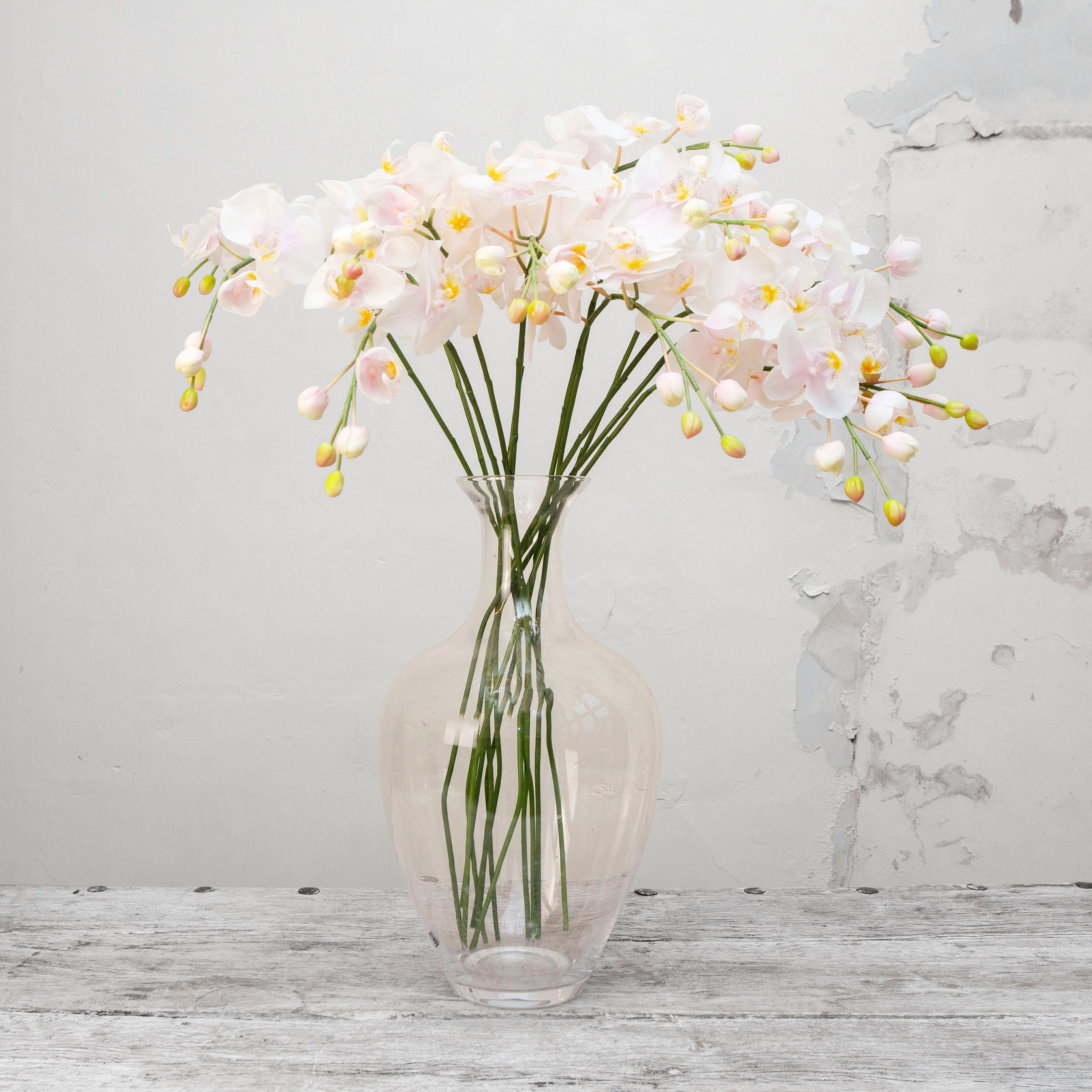Artificial pale pink orchid stem displayed in a vase, showcasing elegant open blooms with soft pink petals, yellow centres and realistic bud detail