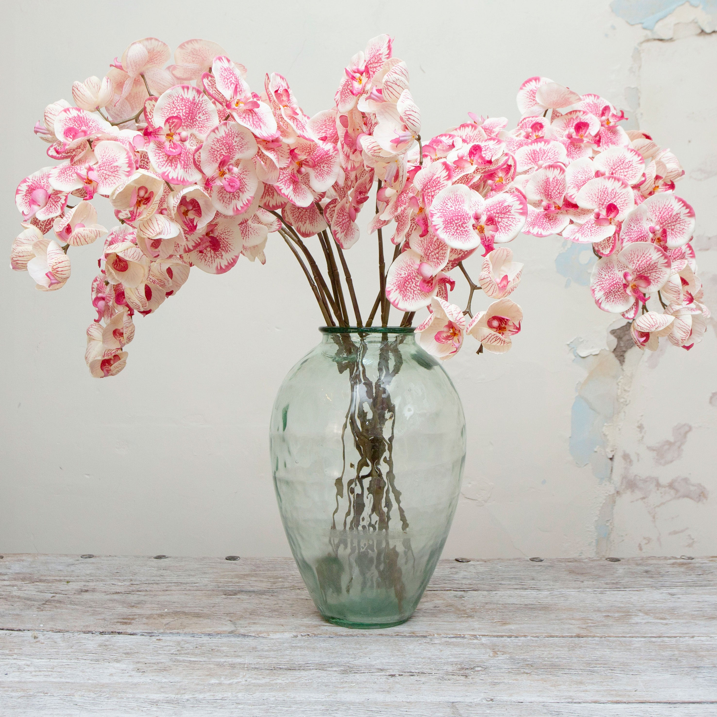 Artificial rose-pink orchid stem displayed in a vase, showcasing arching stems with realistic speckled petals, peach undertones and unopened buds for a natural look.