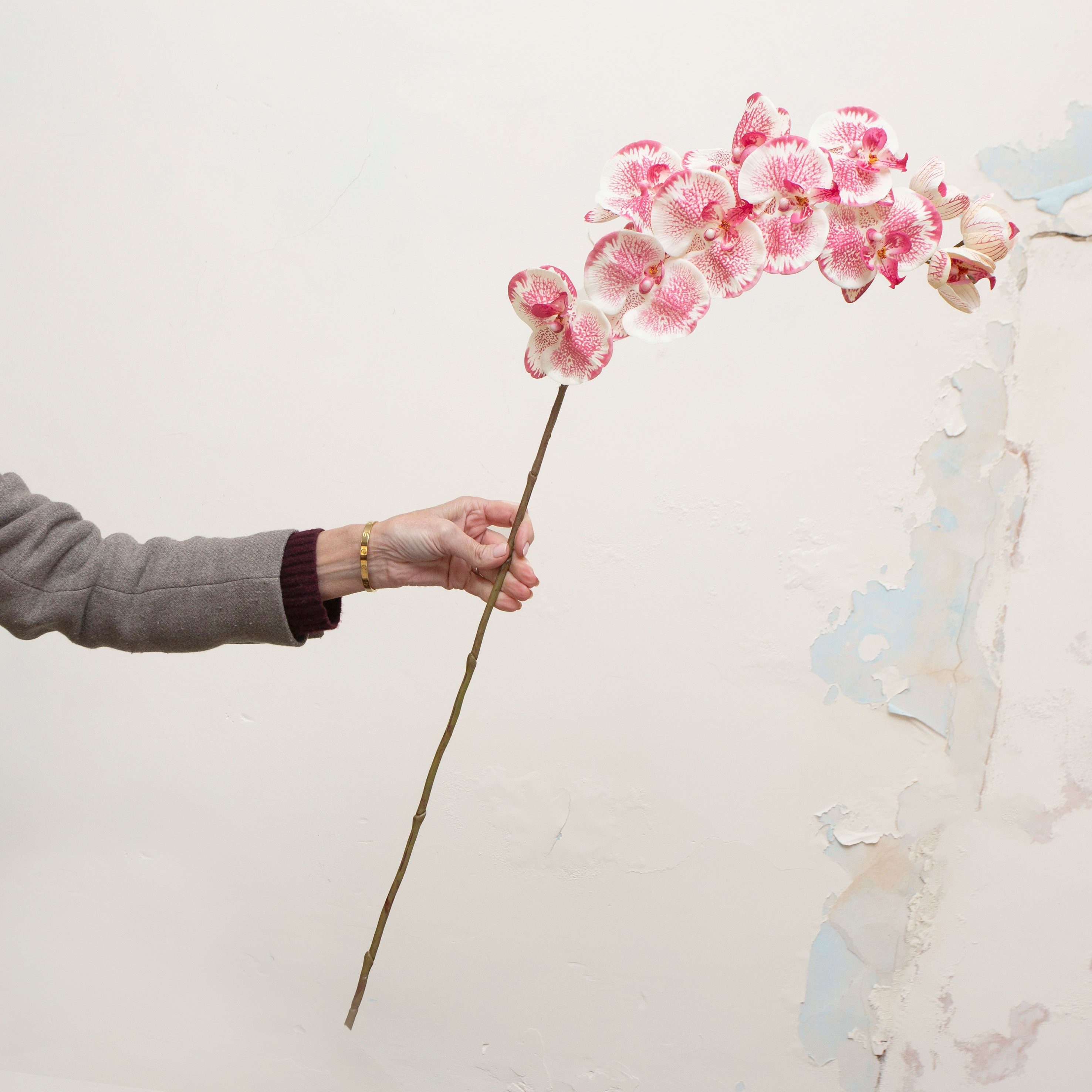 Artificial rose-pink orchid stem being held in hand, featuring softly speckled blooms with warm yellow centres on a gently curved stem