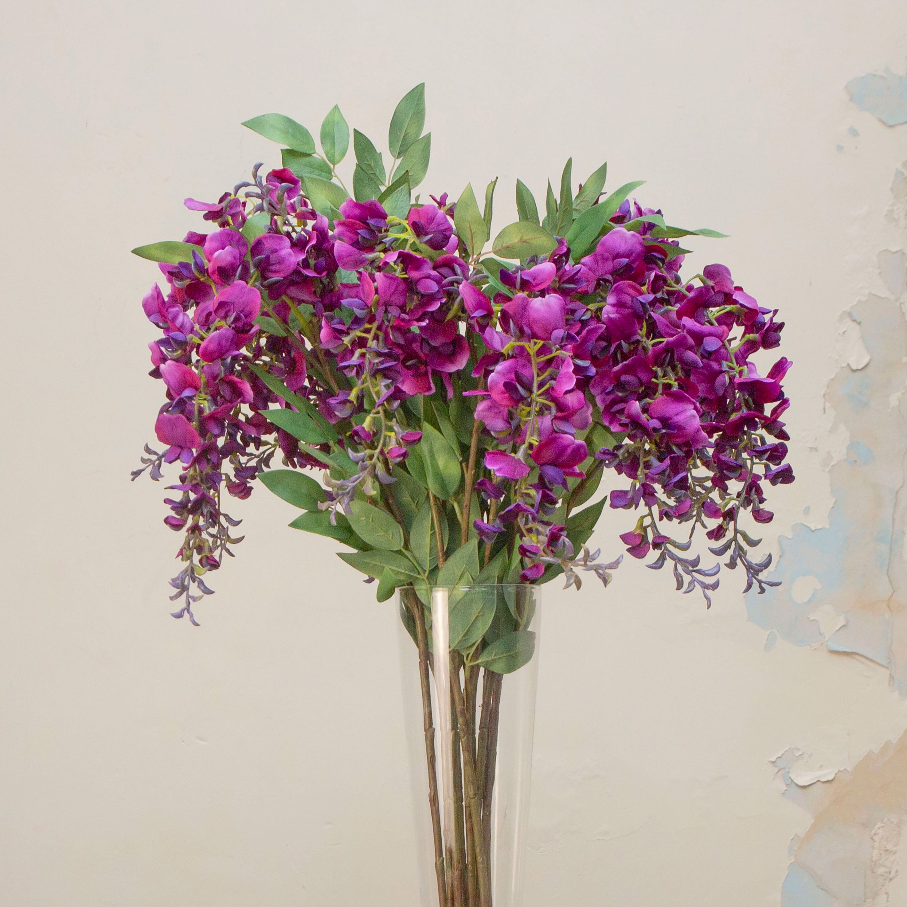 Artificial purple wisteria stem displayed in a vase, showcasing flowing racemes of layered flowers and gentle drape for an elegant, romantic look.