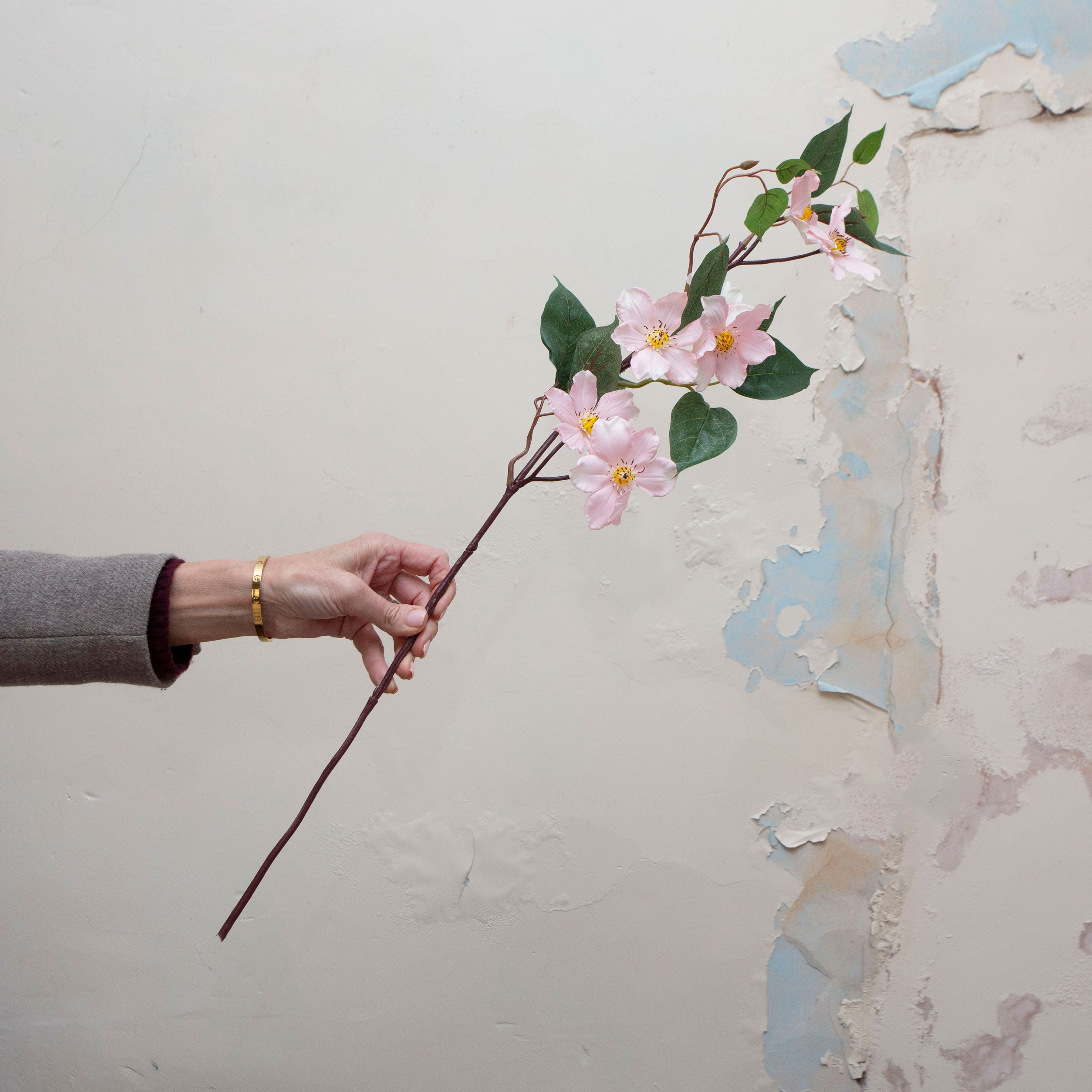 Artificial pale pink clematis stem being held in hand, featuring open star-shaped clematis flowers with soft yellow centres, slender branching stems and realistic green leaves