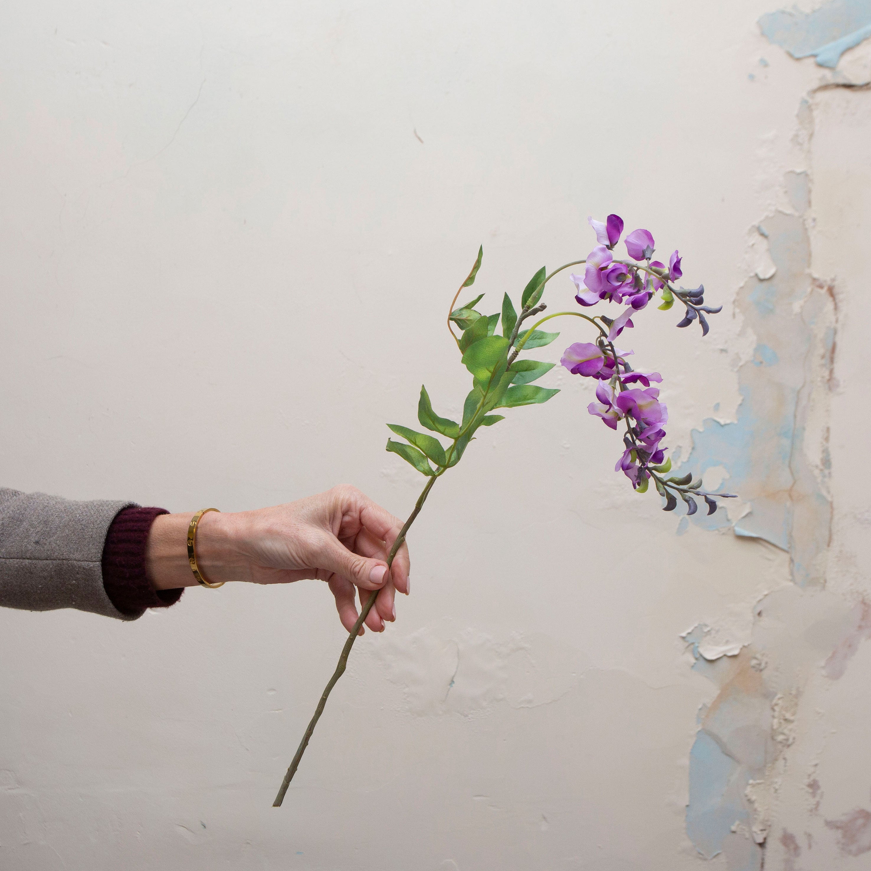 Artificial purple wisteria stem being held in hand, featuring cascading purple blooms with soft green foliage on a slender stem