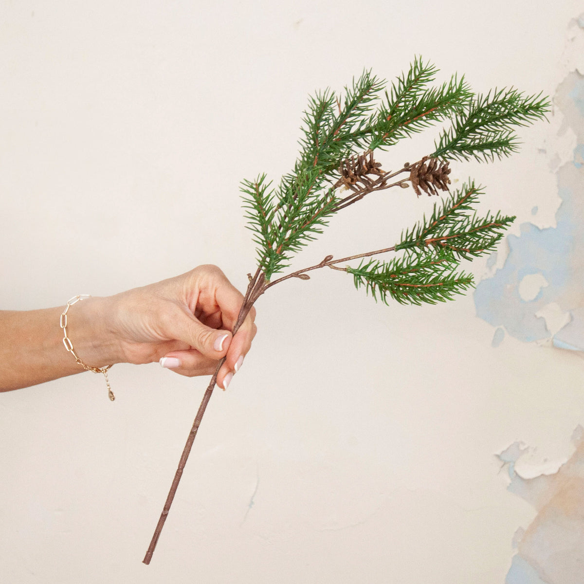 Hand holding artificial Pine Cone Stem with realistic green pine foliage and brown pine cones