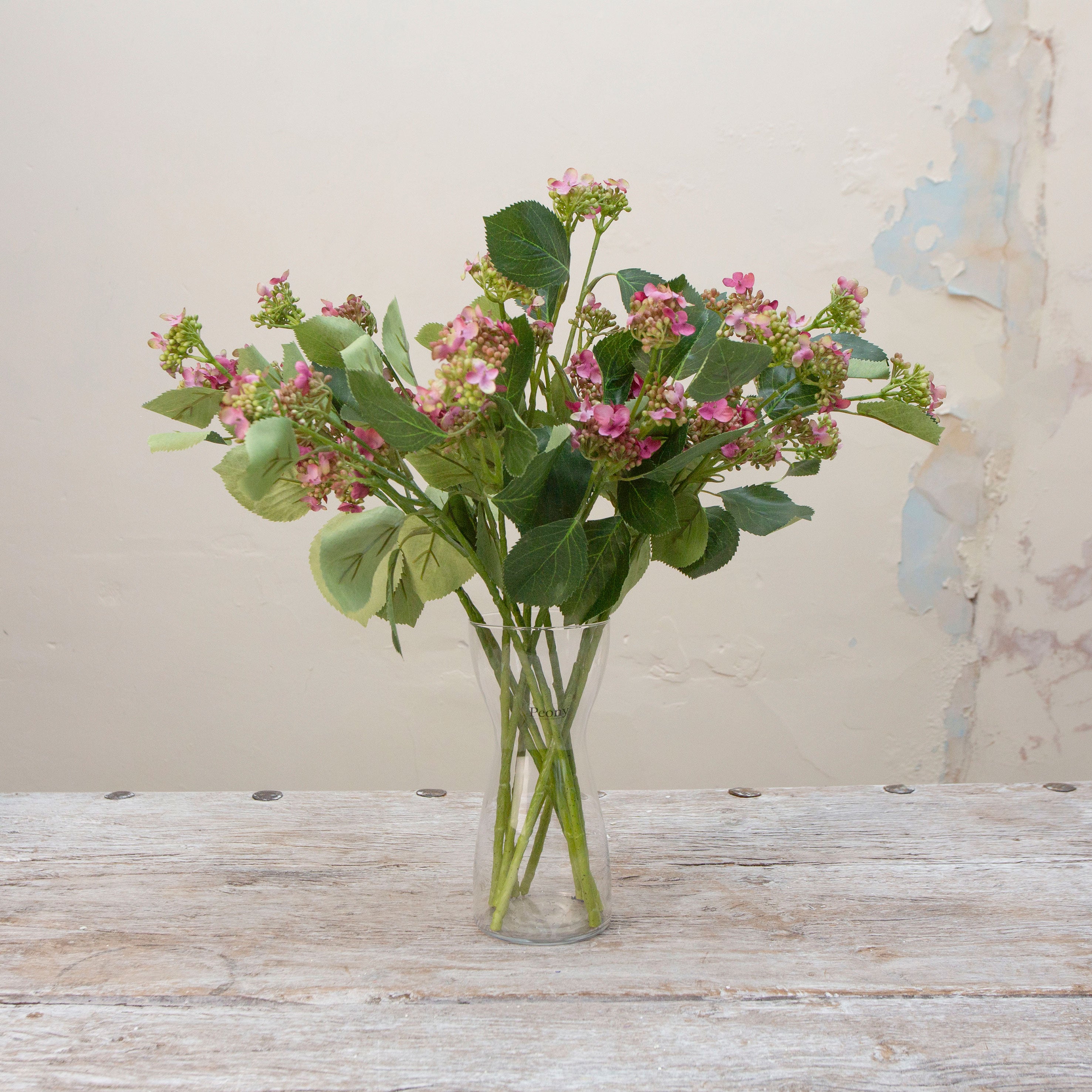 Artificial pink flowering viburnum stem displayed in a vase, showcasing delicate pink bud clusters, gentle branching and realistic green foliage