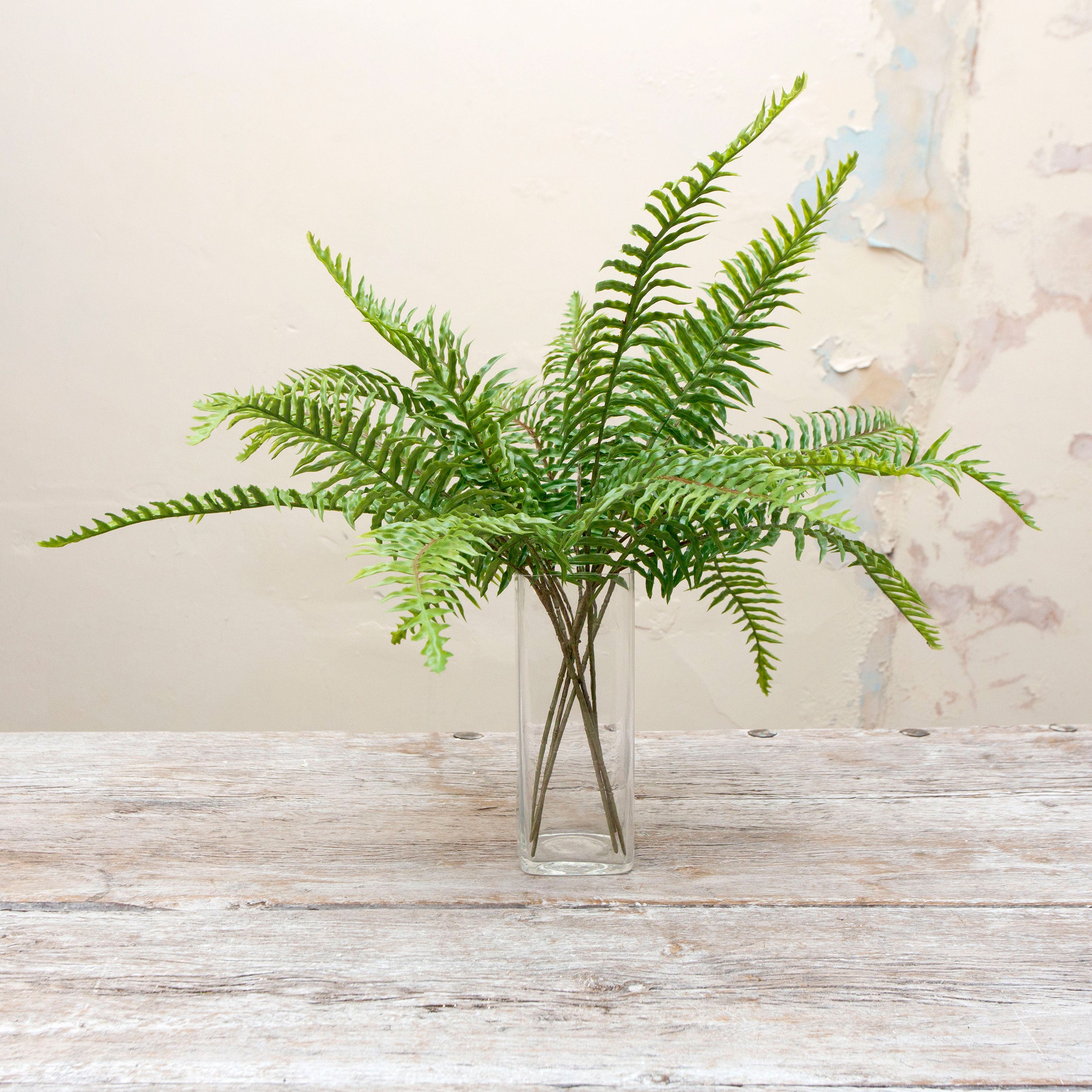 Artificial green fern spray stems displayed together in a clear glass vase for styling purposes.