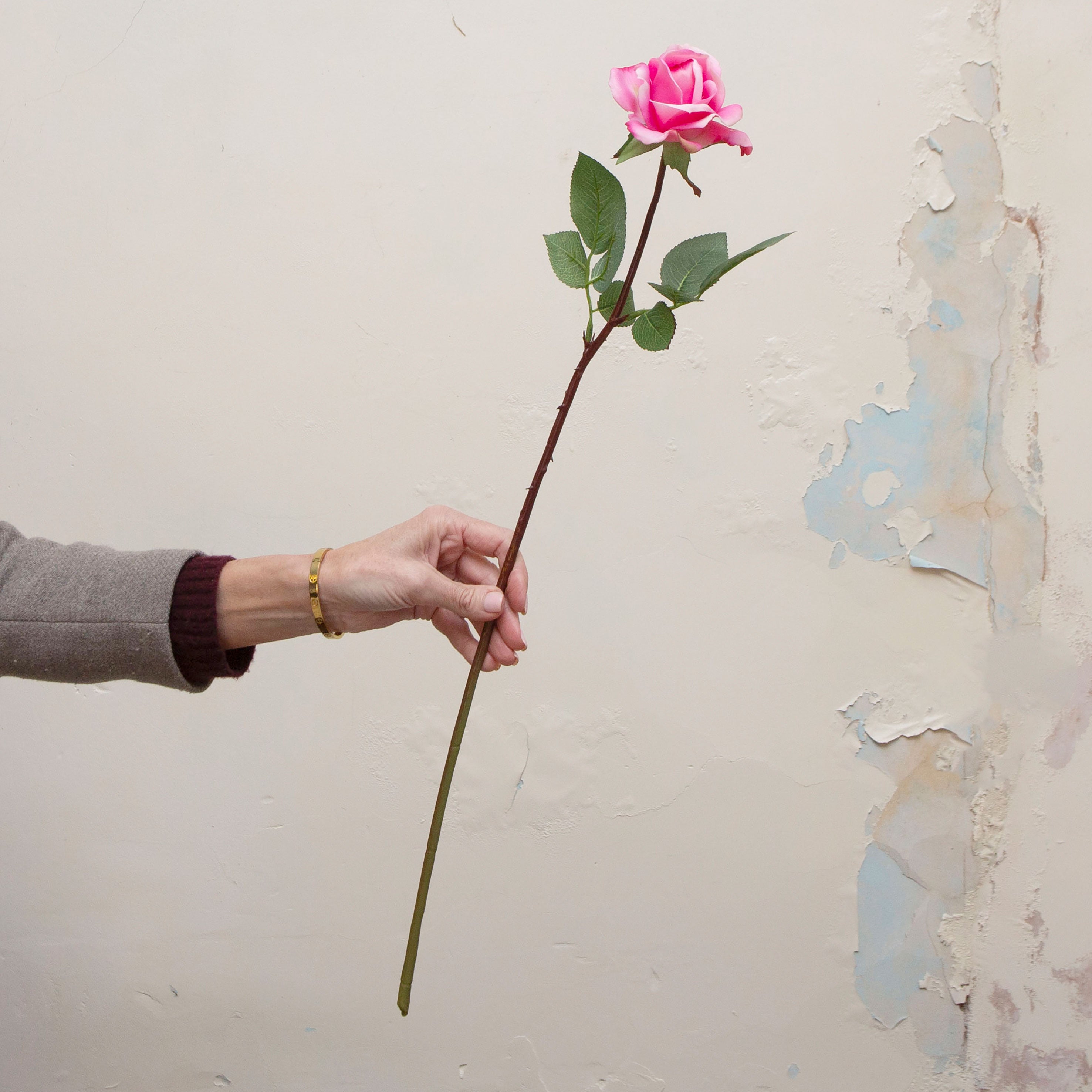 Artificial bright pink rose stem being held in hand, featuring a classic rose bloom with vibrant pink petals and realistic green foliage on a slender stem