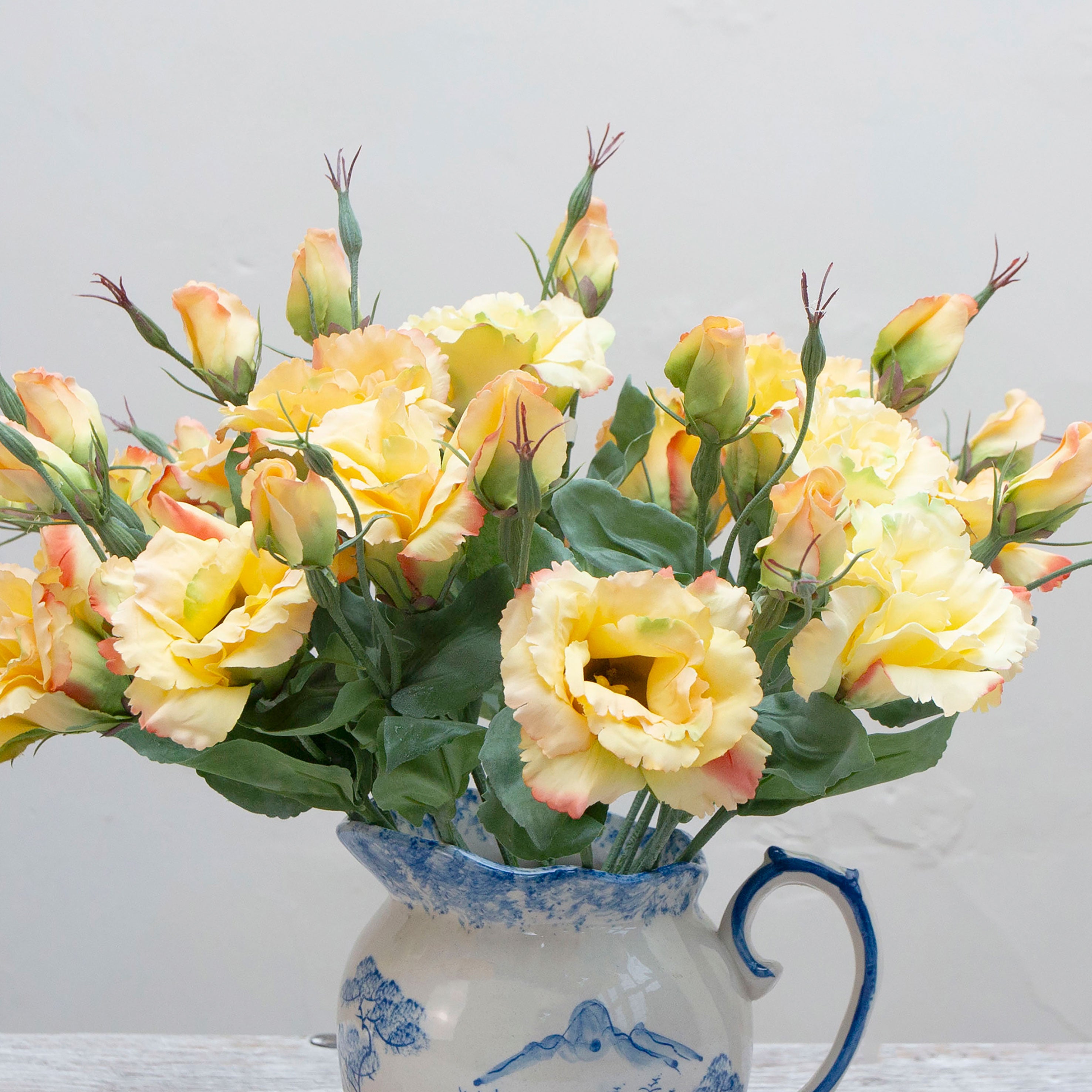 Close-up of artificial yellow lisianthus flowers showing layered petals with soft peach edging.