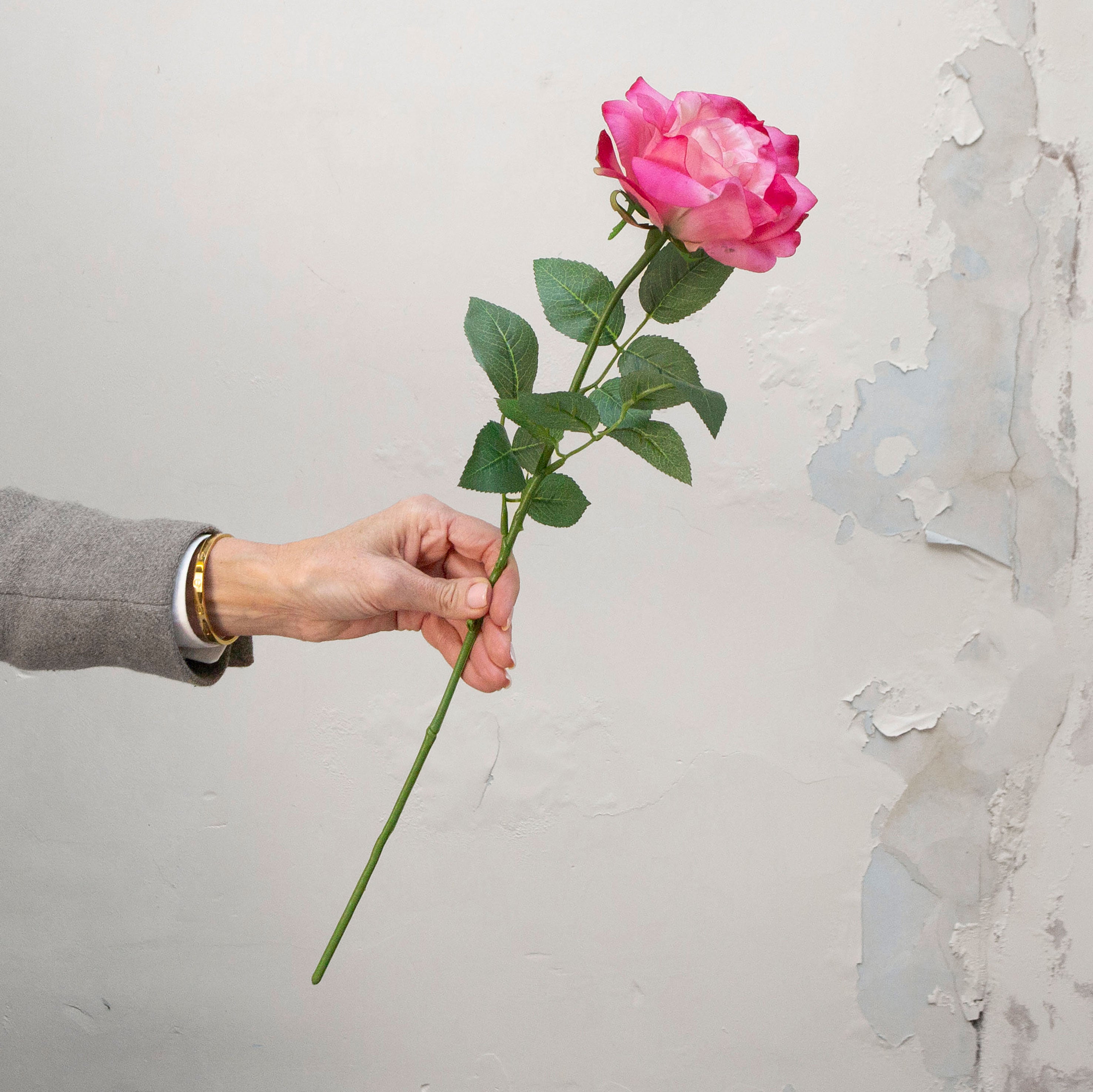 Artificial pink rose stem held in hand, featuring layered petals and realistic green foliage