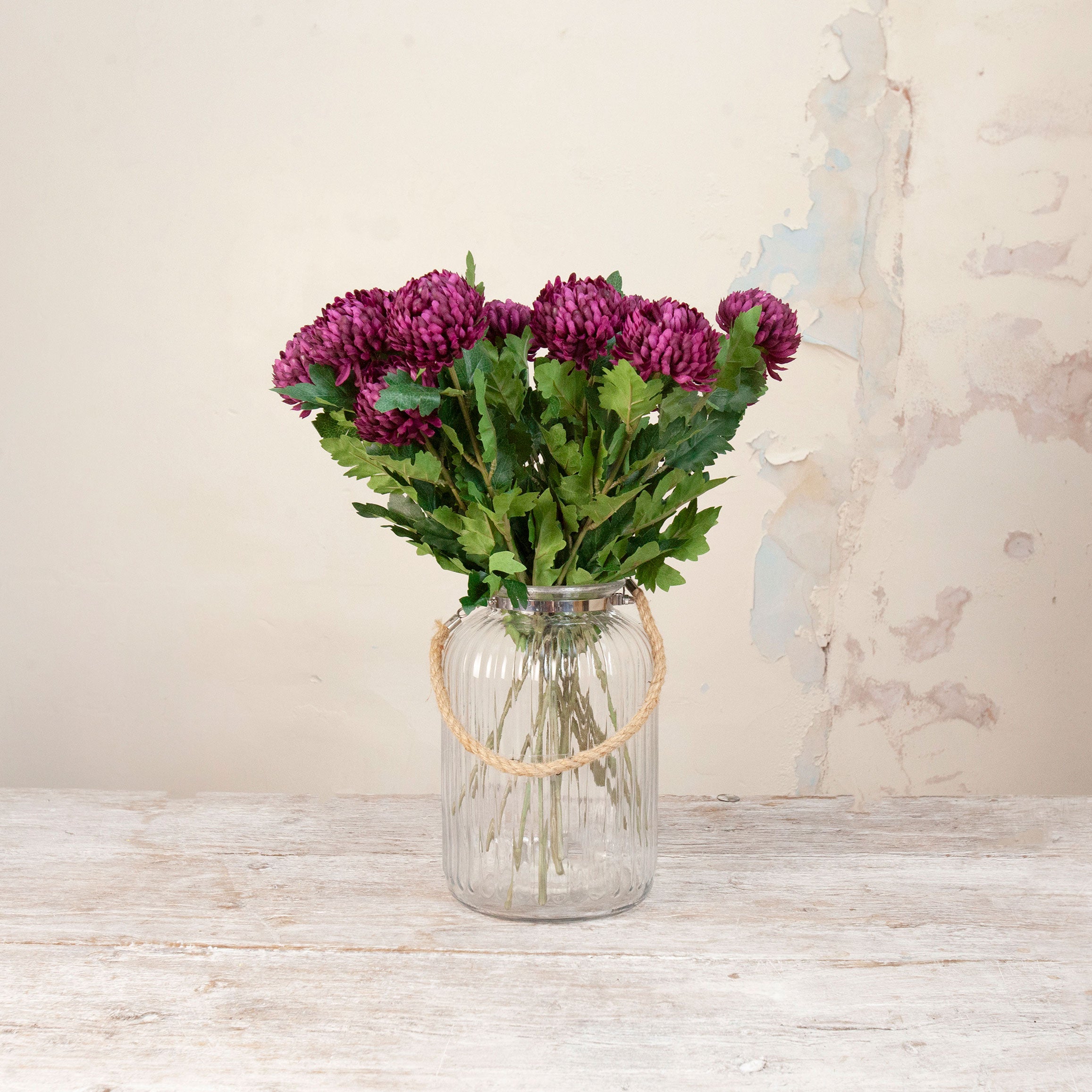 Artificial Chrysanthemum Stems with rich burgundy blooms and realistic green foliage displayed in a clear ribbed glass vase