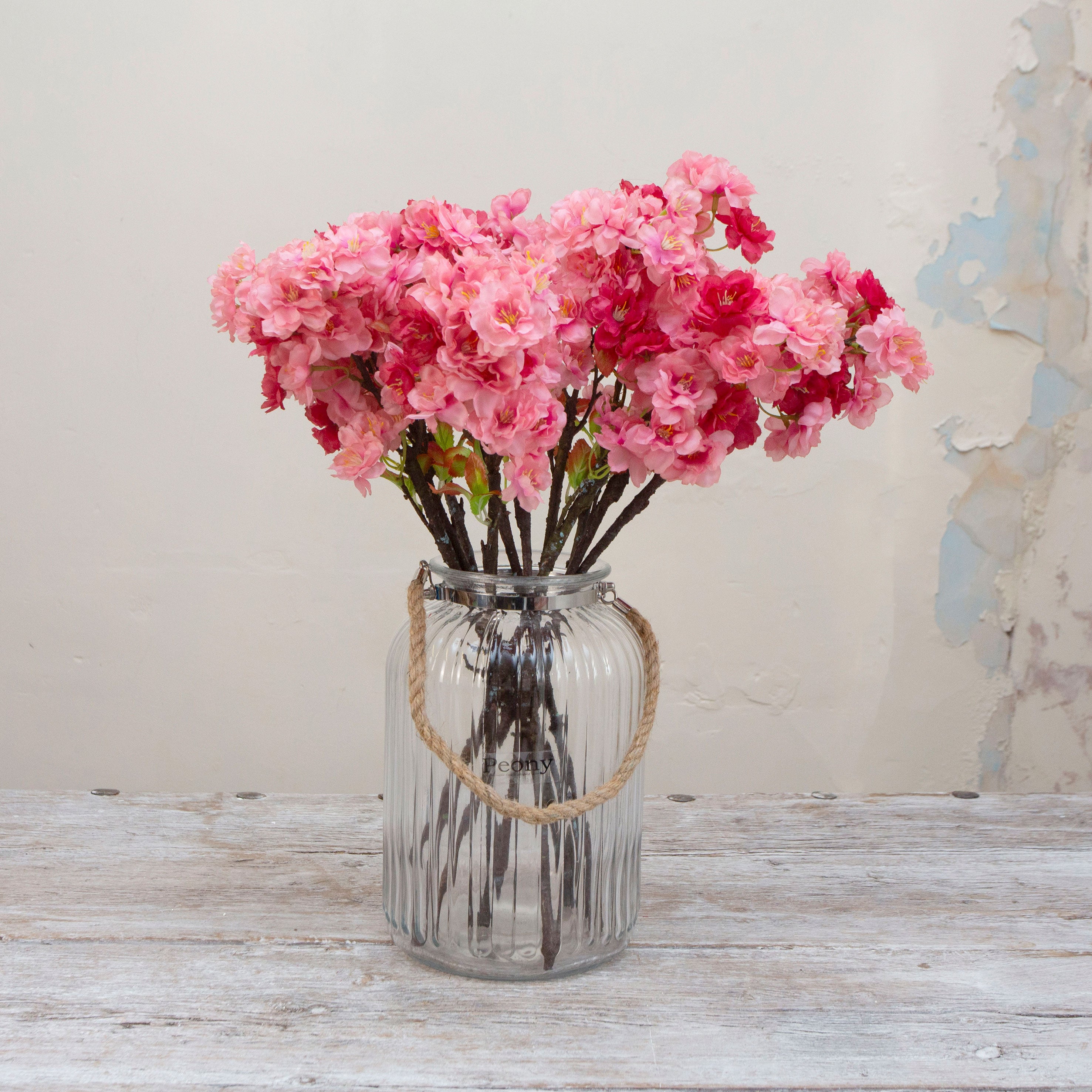 Artificial pink cherry blossom spray stems with layered blossoms, displayed together in a glass vase for display.
