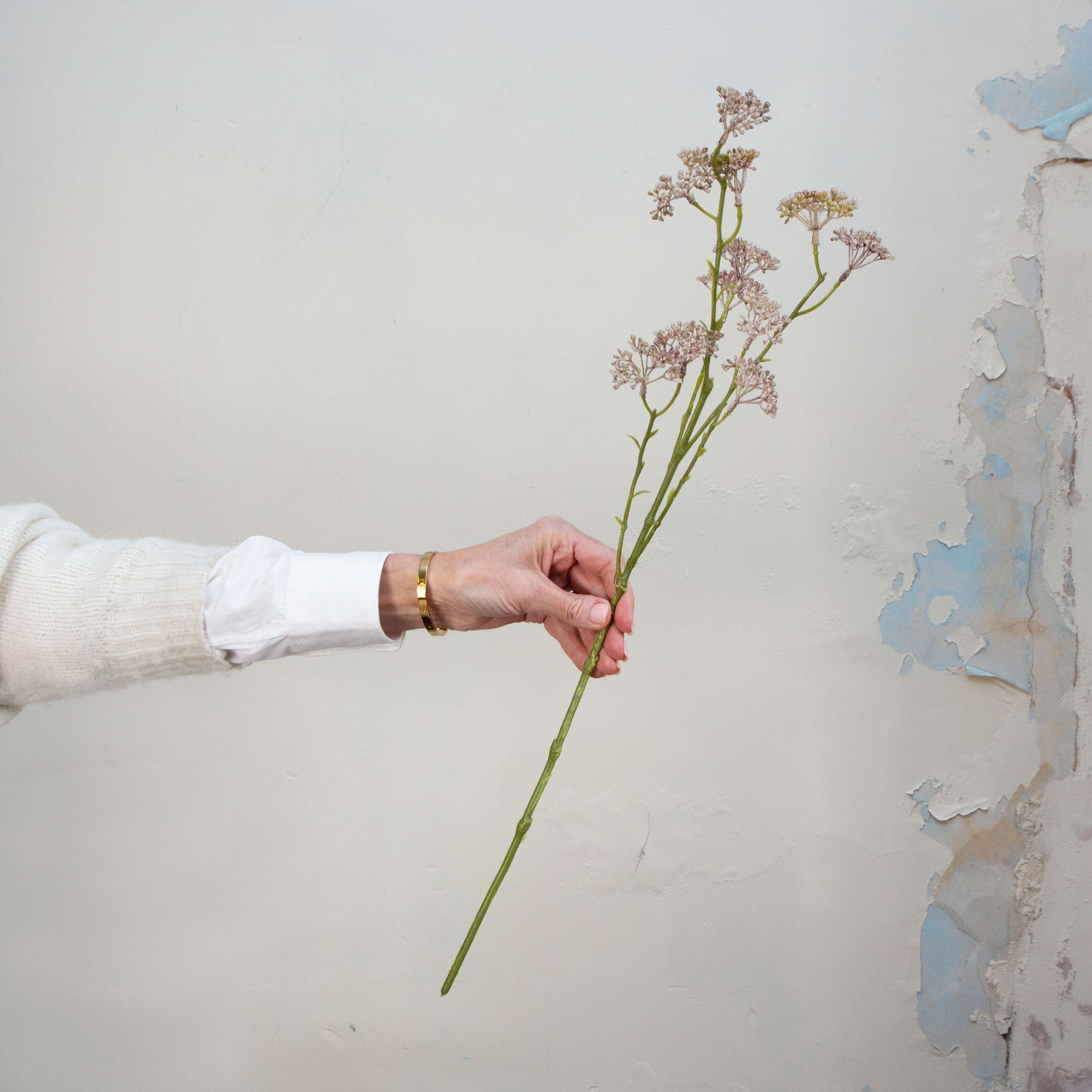 Artificial dusky mauve pink patrinia spray stem held in hand, featuring delicate clustered flowers on fine branching stems.