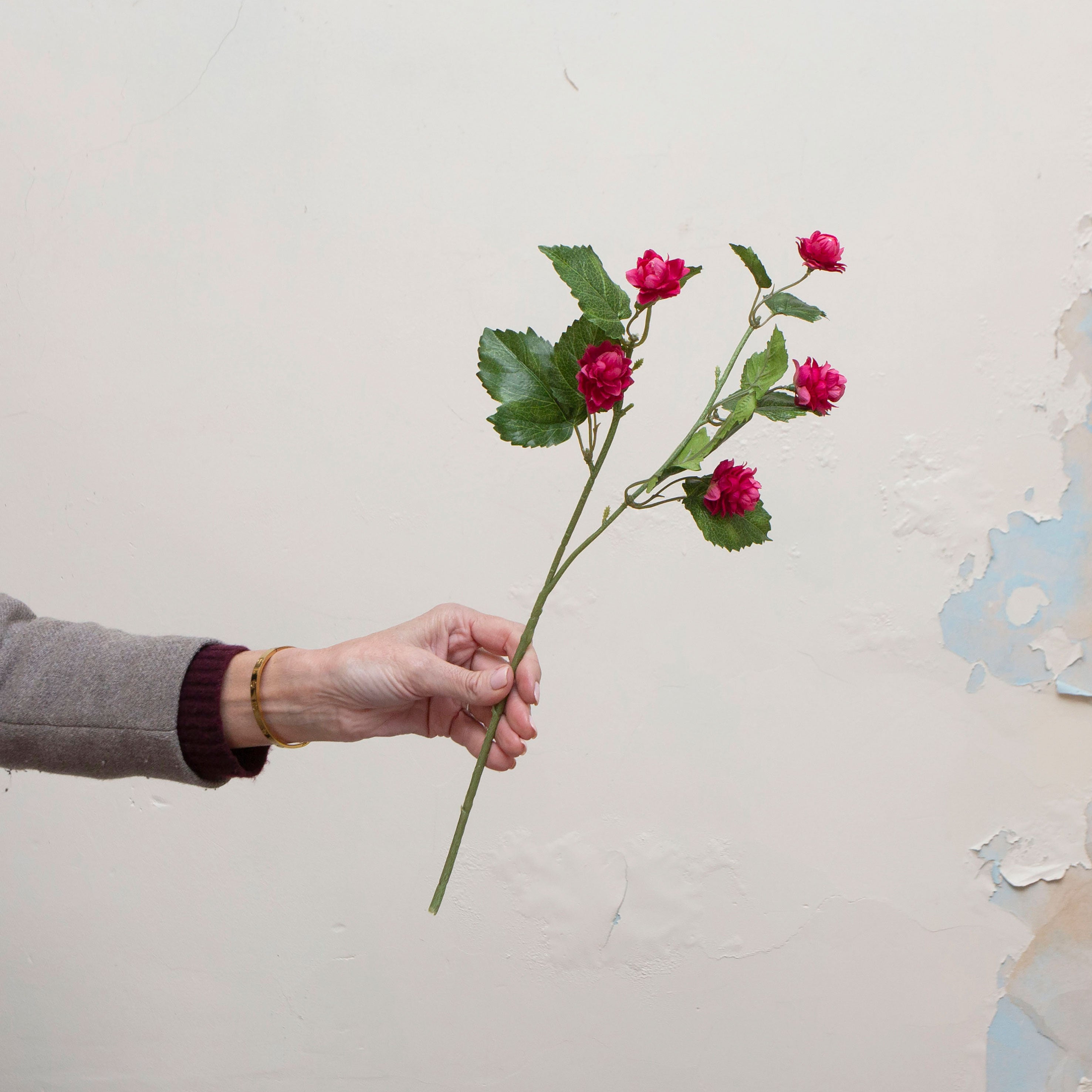 Artificial fuchsia hop spray stem held in hand, featuring layered pink flowers and realistic green leaves.
