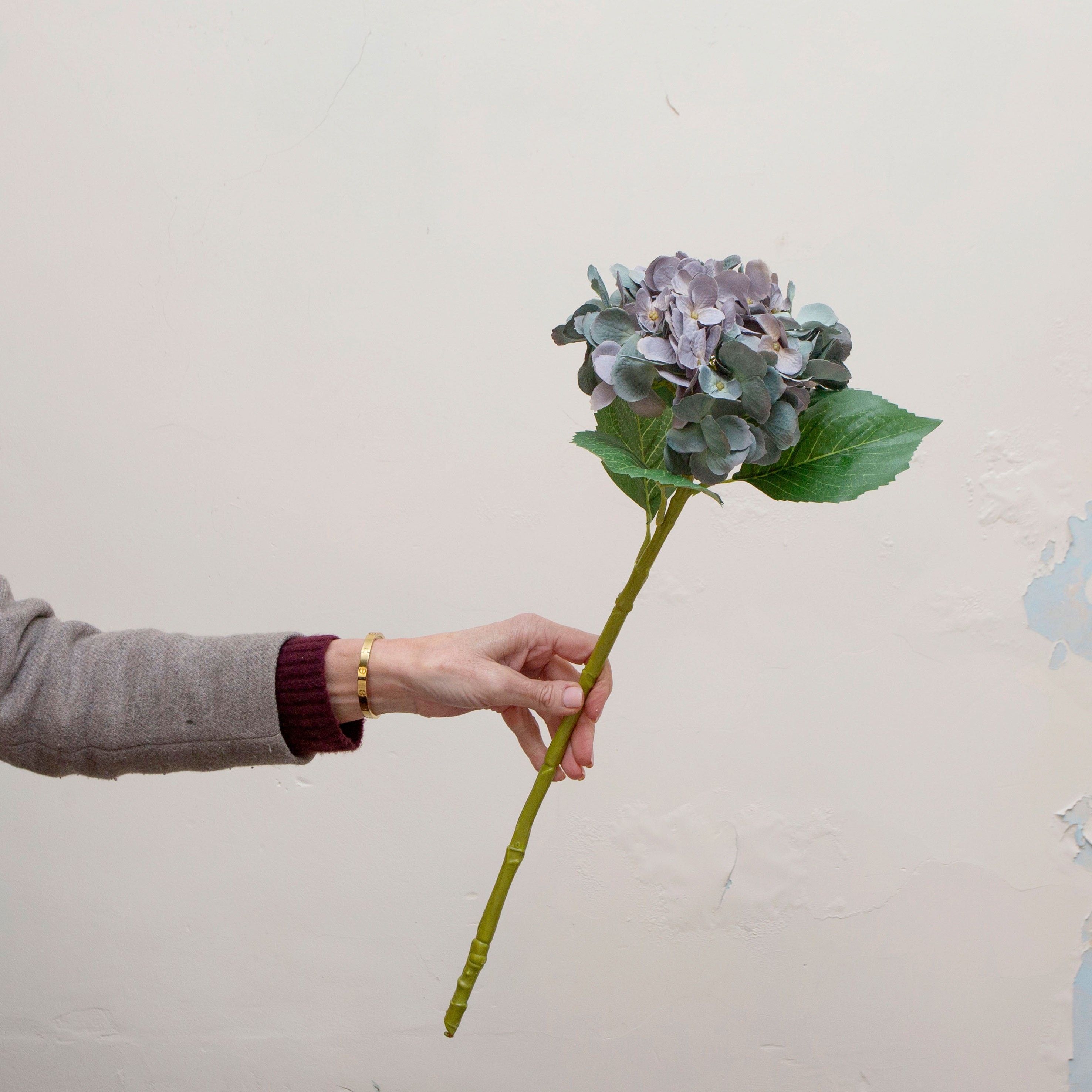 Single artificial hydrangea stem with blue-purple bloom and green foliage.