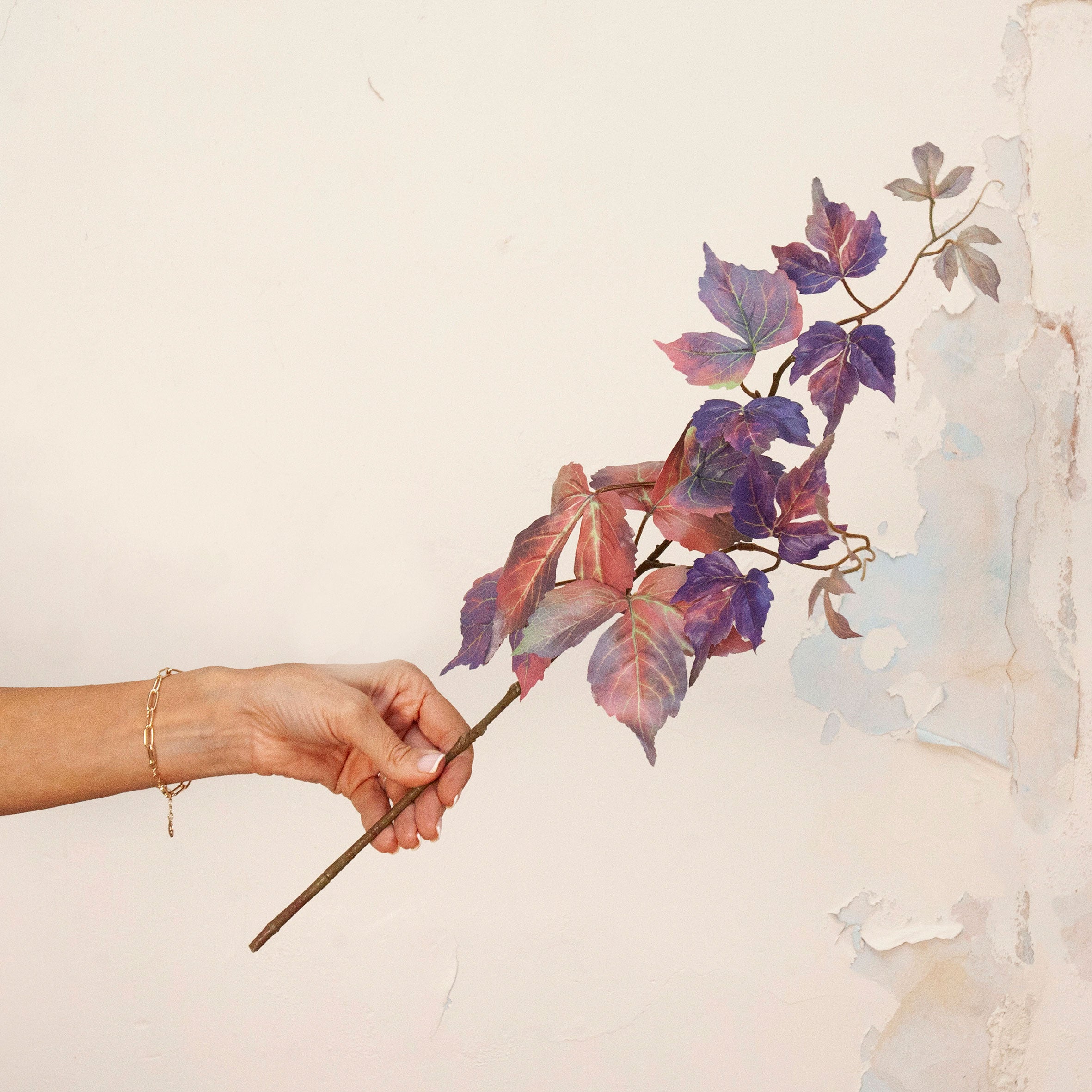 Hand holding Artificial Leaf Foliage Stem with trailing purple, burgundy and muted autumn-toned leaves