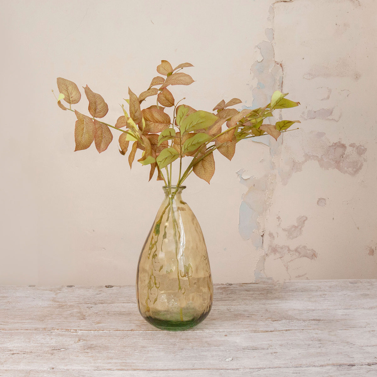 Artificial Salal Leaf Stems with green, bronze and warm brown foliage displayed in an amber-tinted glass vase