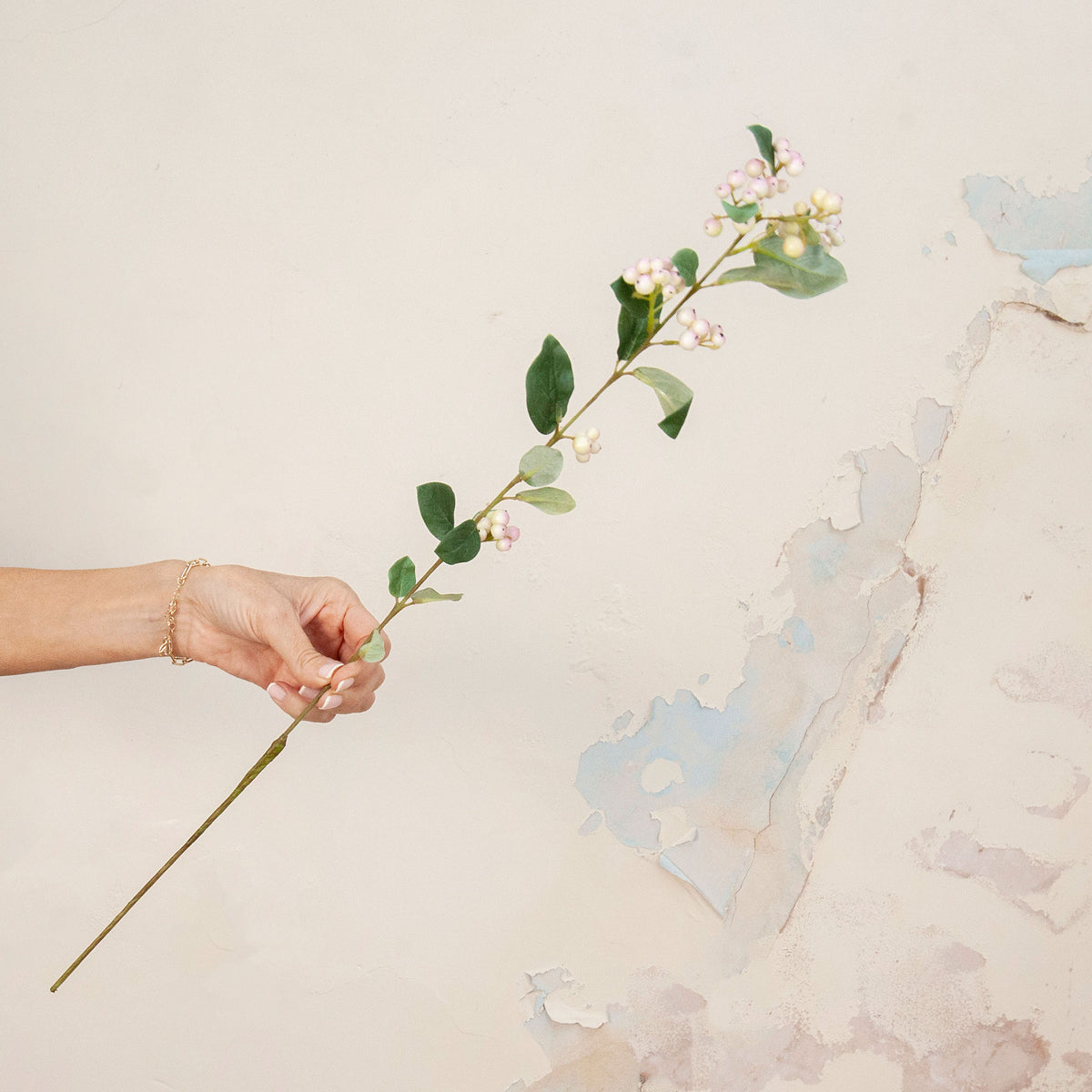 Hand holding Artificial Snowberry Stem with soft pink and white berry clusters and realistic green foliage