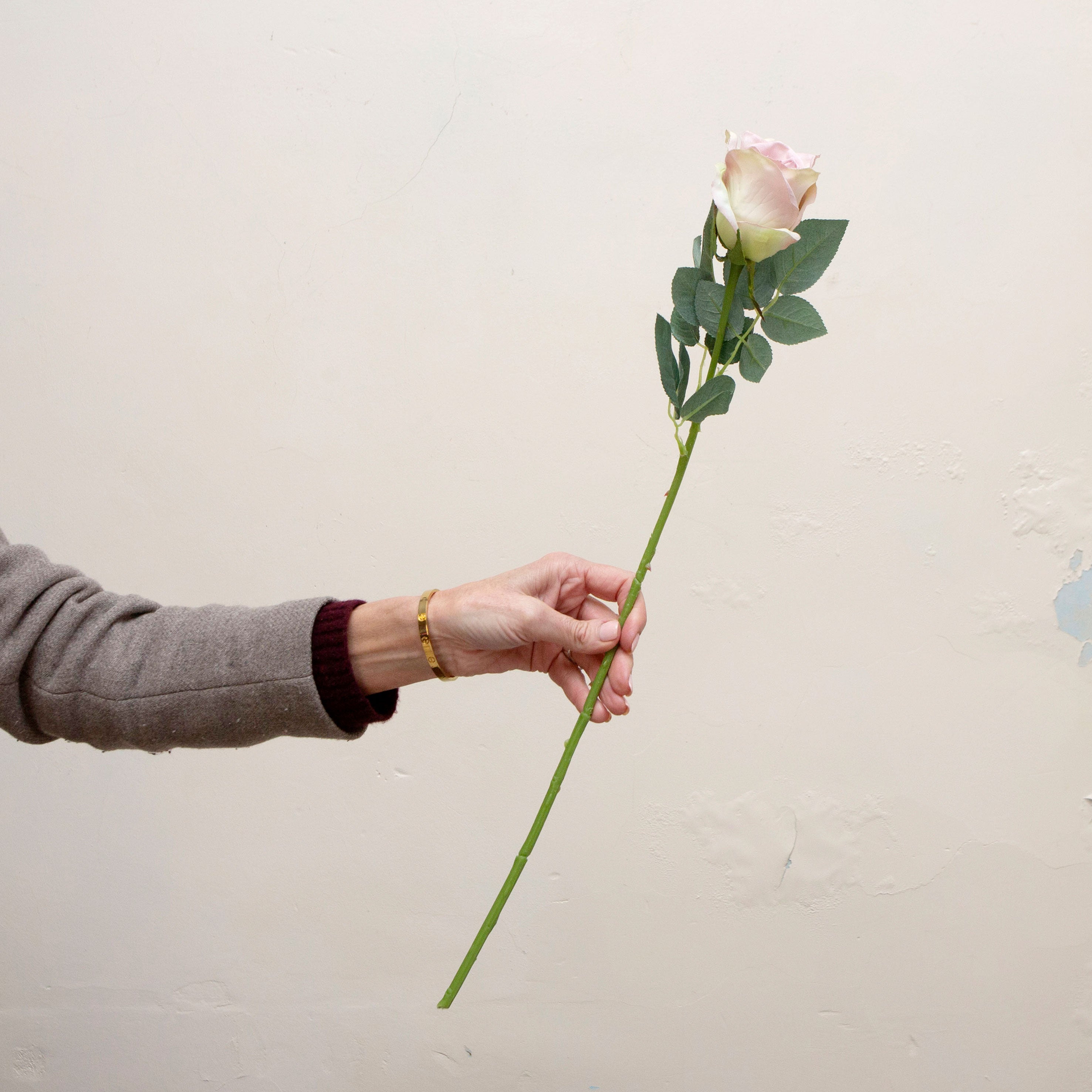 Artificial dusky pink rose stem held in hand, featuring layered petals and realistic green foliage.