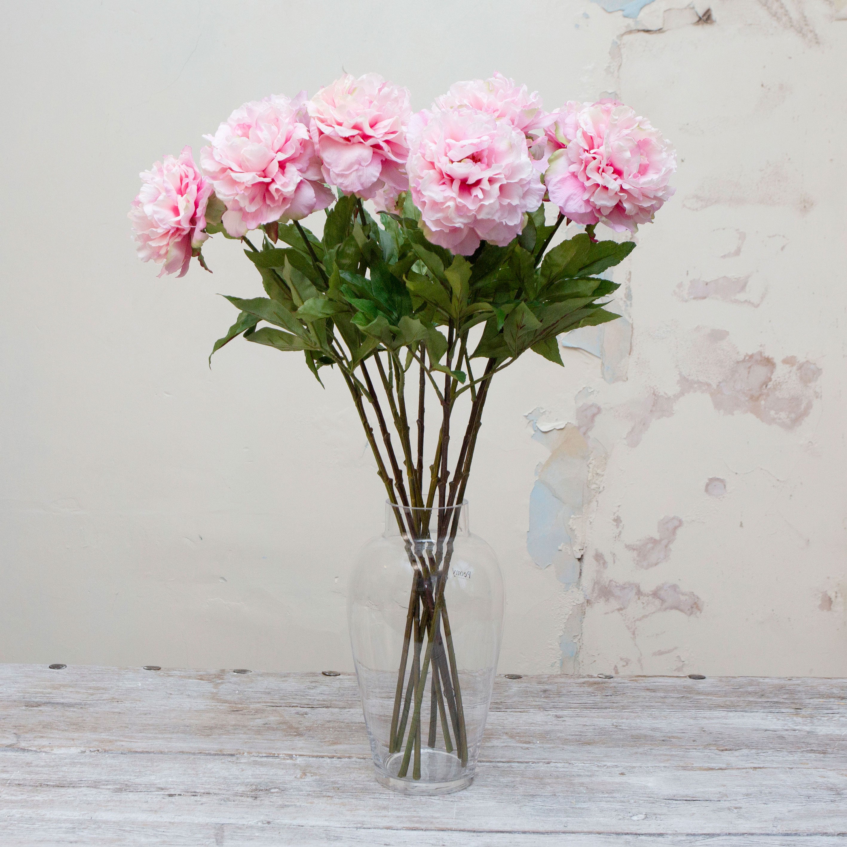 Artificial pink peony stems with green leaves displayed in vase