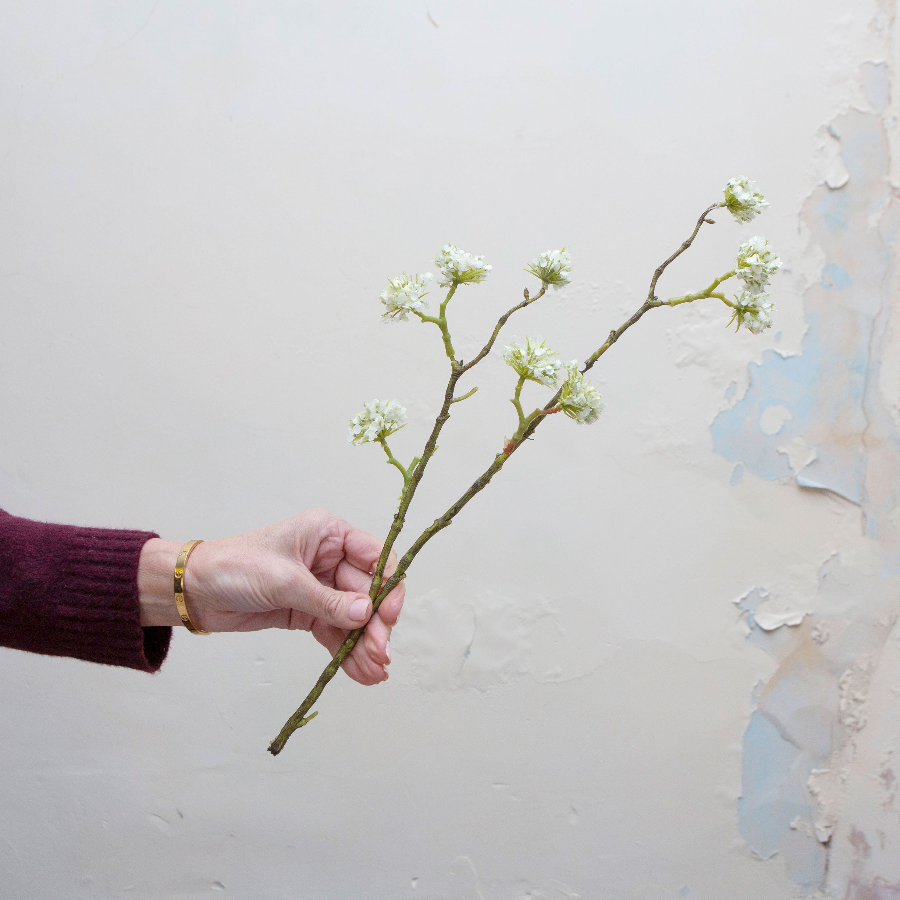 Artificial white buddleia spray stem held in hand, featuring clustered flowers on branching stems