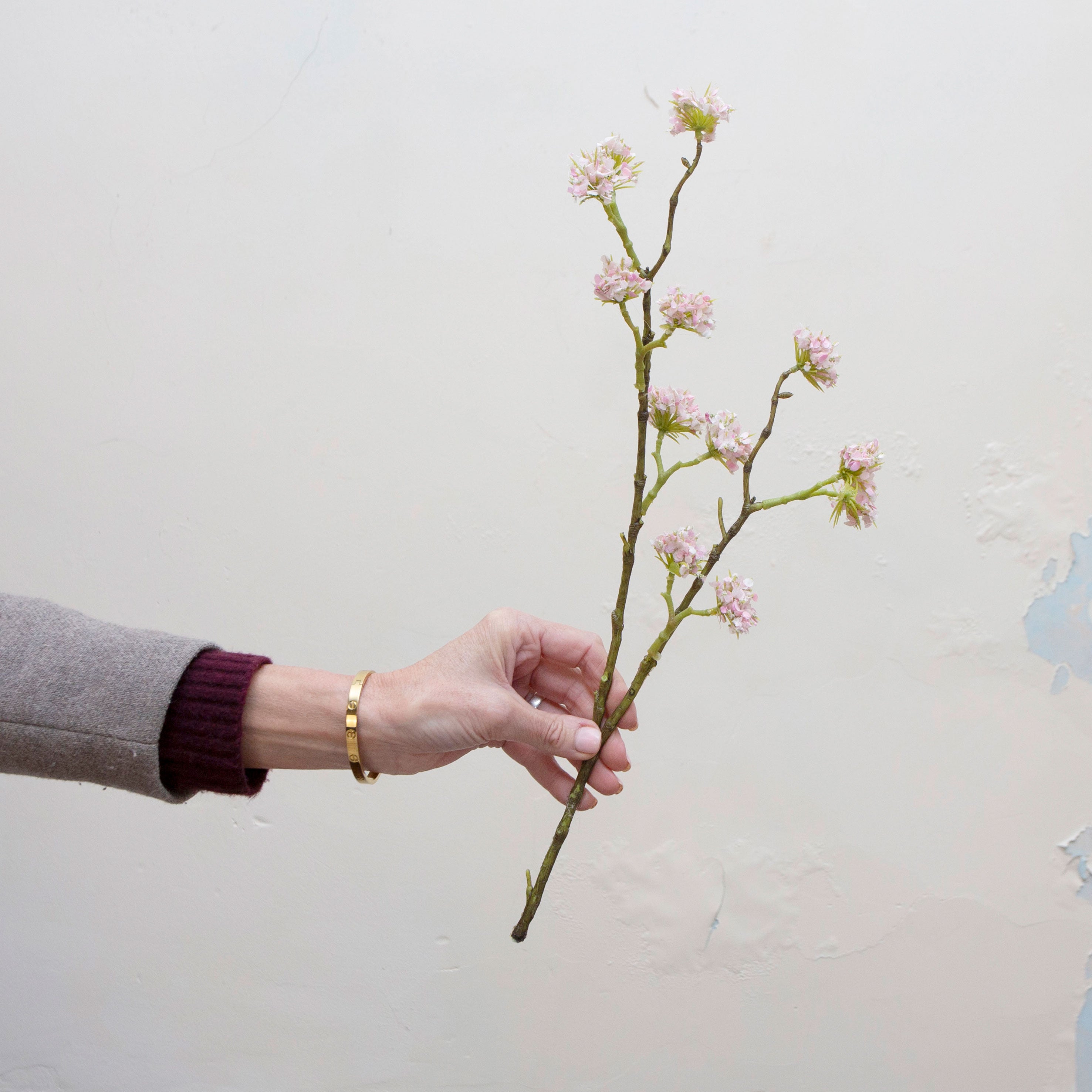 Artificial pale pink buddleia spray stem held in hand, featuring clustered flowers on branching stems