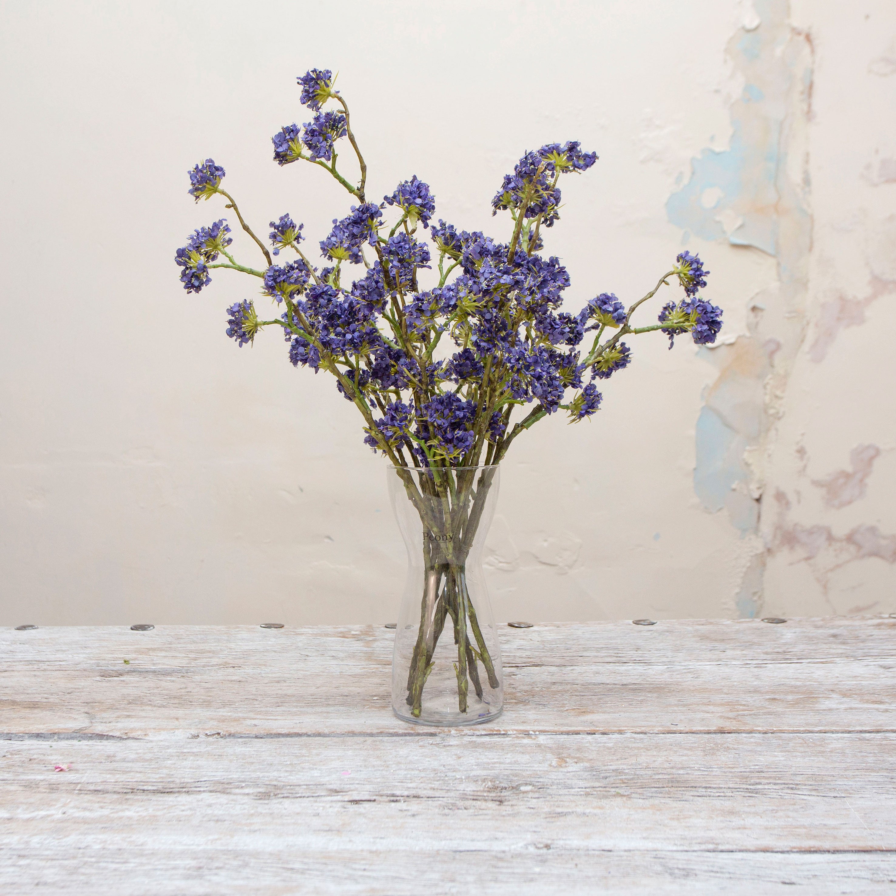 Artificial purple-blue buddleia spray stems displayed together in a vase for styling purposes