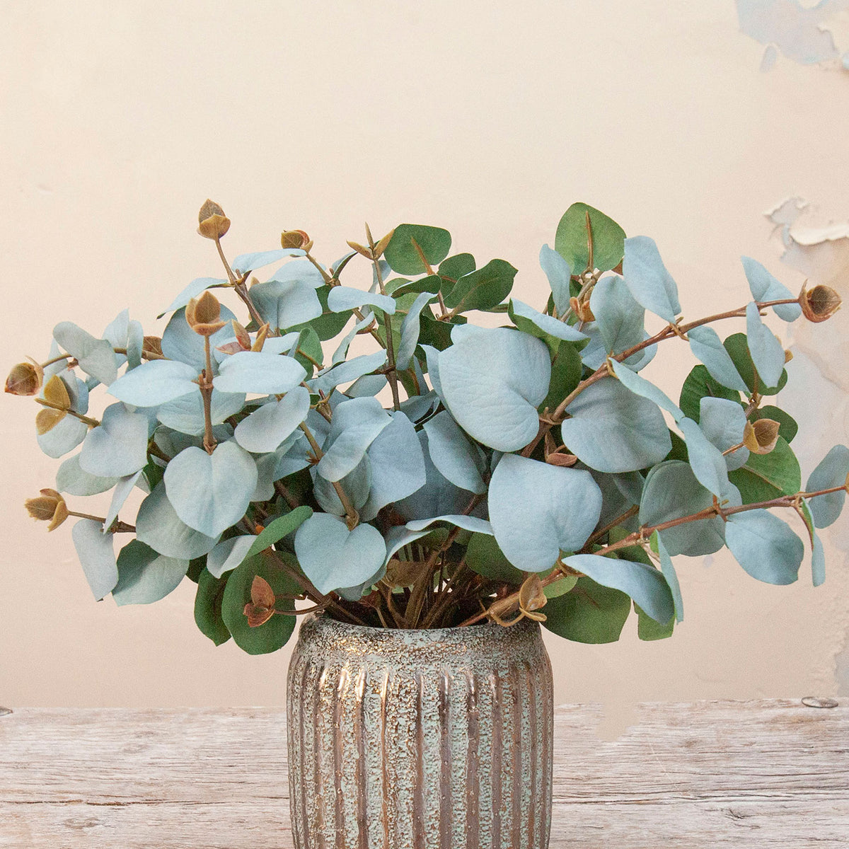Close up Artificial Eucalyptus Bunch Stems with soft blue-green rounded leaves and natural brown seed pods displayed in a textured metallic vase