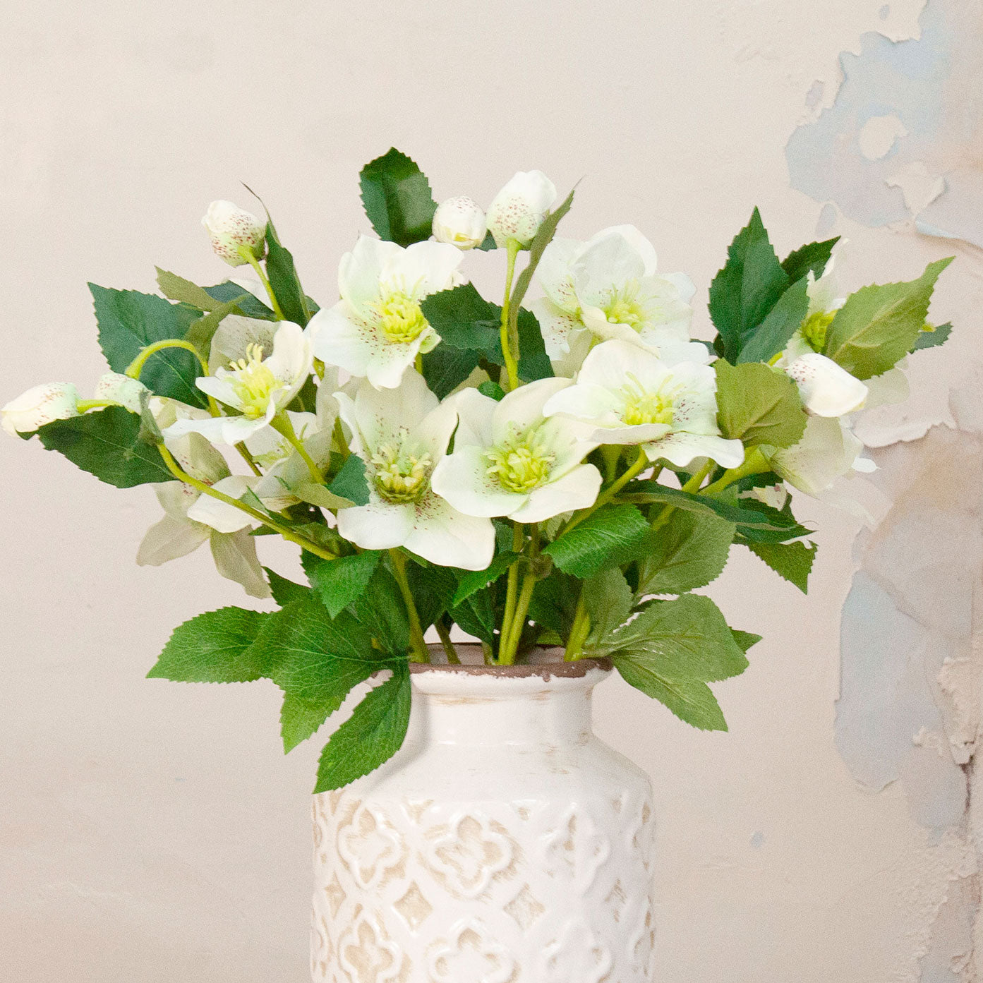 Close up Artificial Hellebore Stems with delicate white flowers, soft green centres, buds and realistic green foliage displayed in a textured white ceramic vase