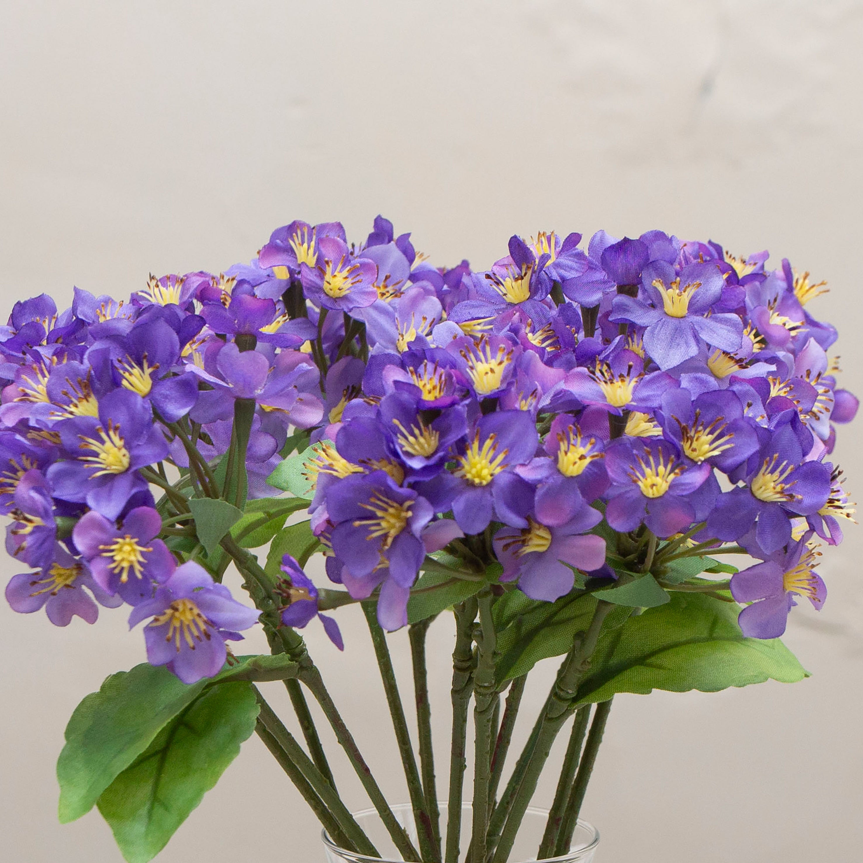 Close-up of artificial purple blossom stems with yellow centres and green leaves