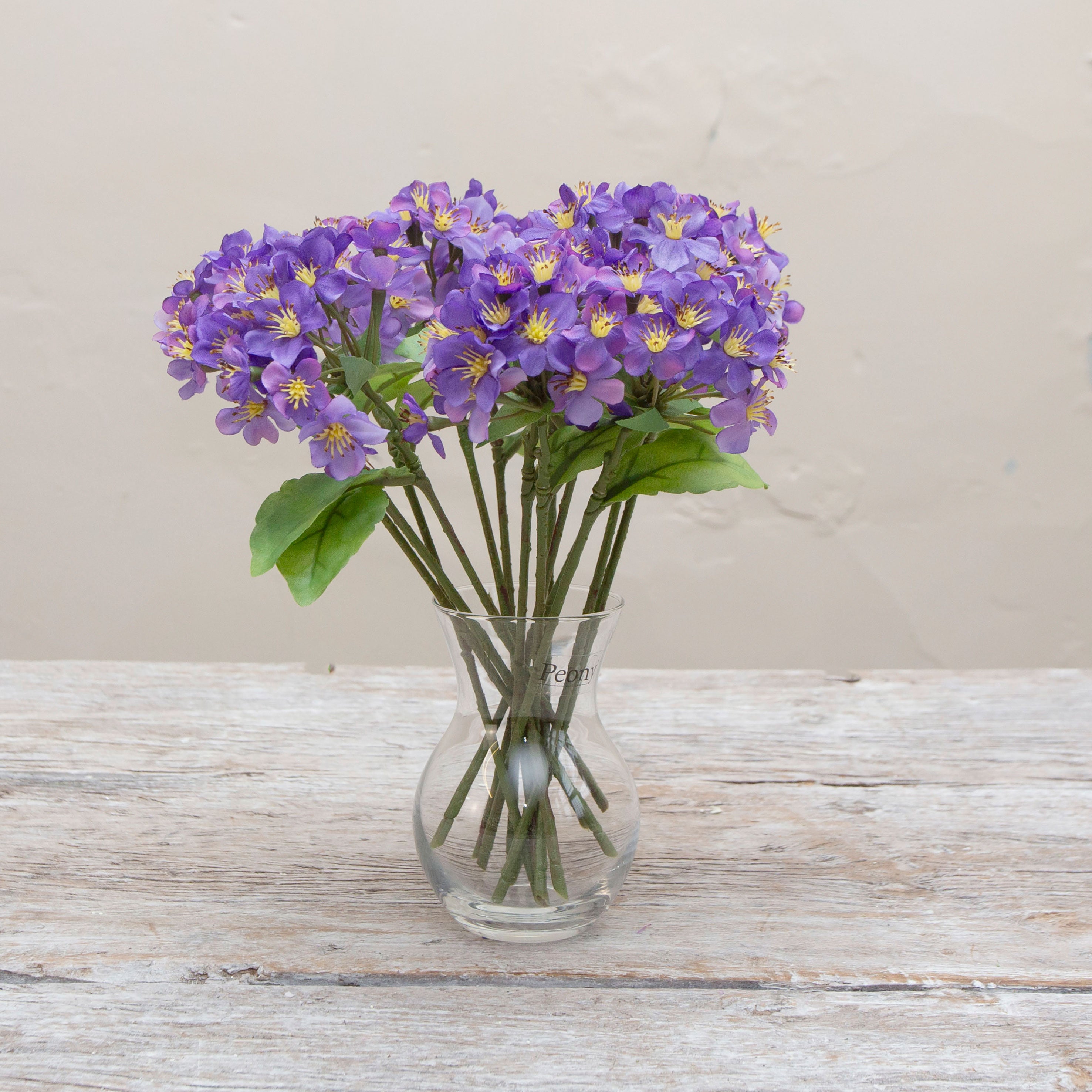 Artificial purple Blossom pick stems with yellow centres displayed in a glass vase