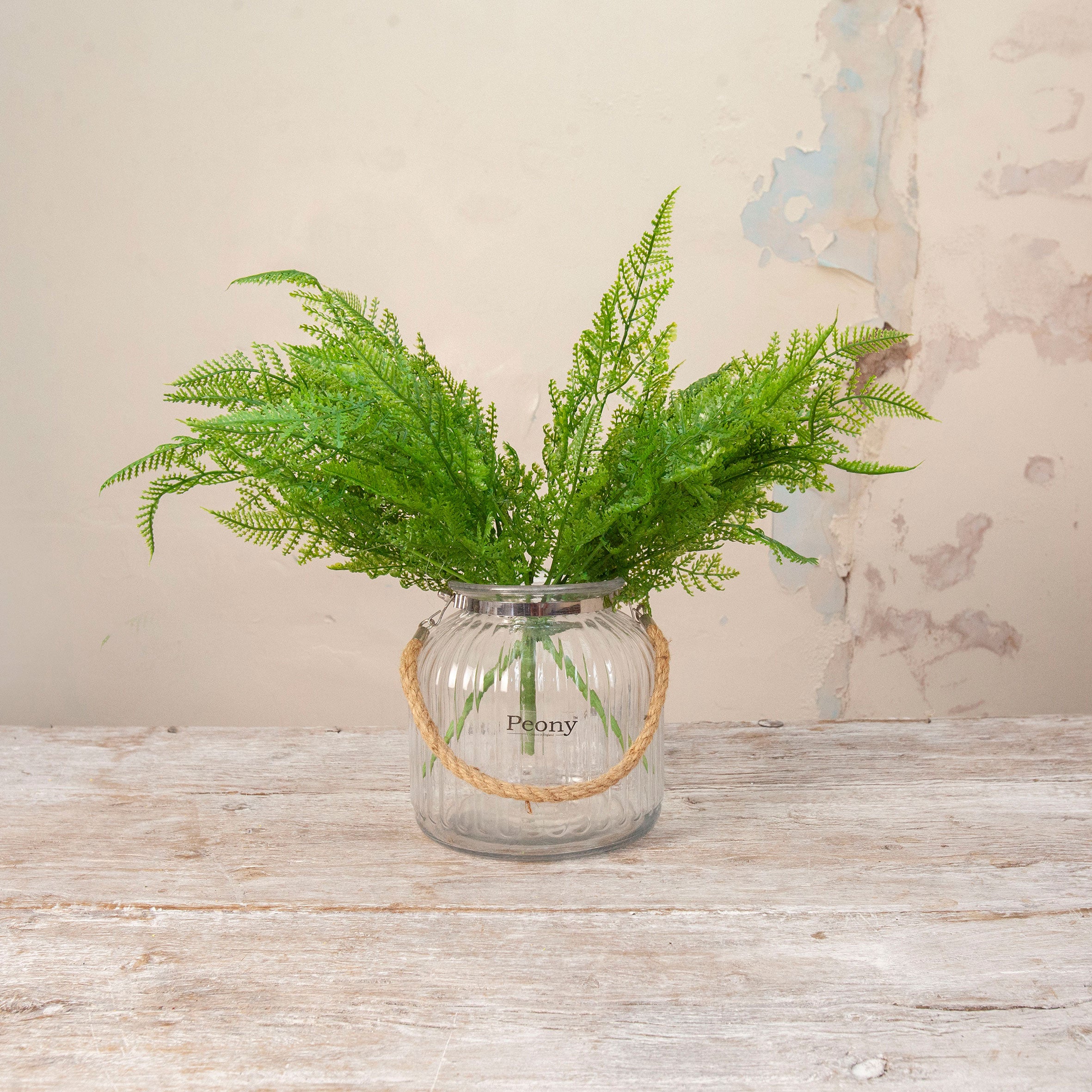 Artificial Fern Bush Stems with lush, feathery green fern foliage displayed in a clear ribbed glass vase with rope handle