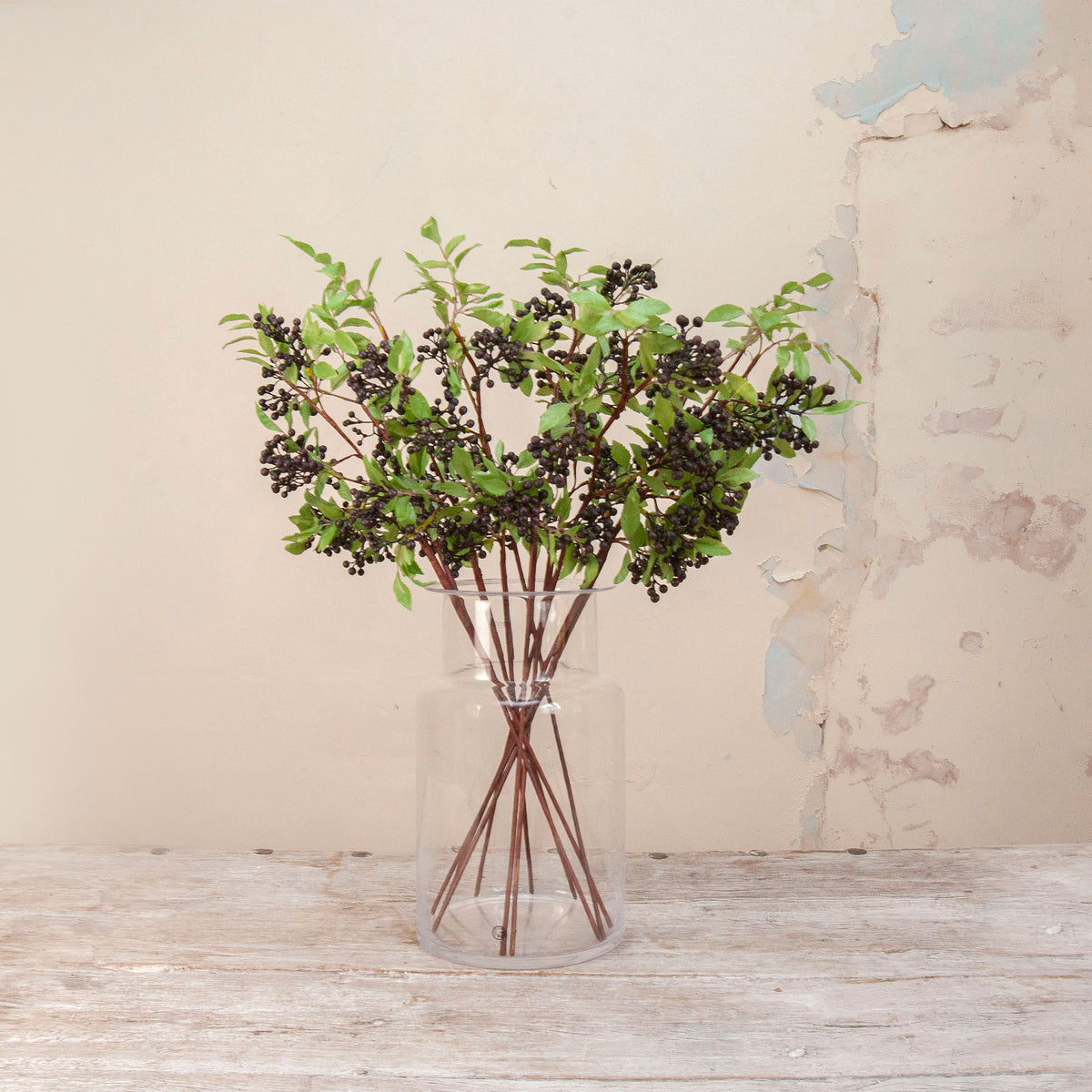 Artificial Berry Stems with clusters of dark purple-black berries, fresh green leaves and natural brown branches displayed in a clear glass vase